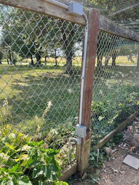 Fence with chain link, wood posts, and electrical boxes. Green grass and plants are in the background.