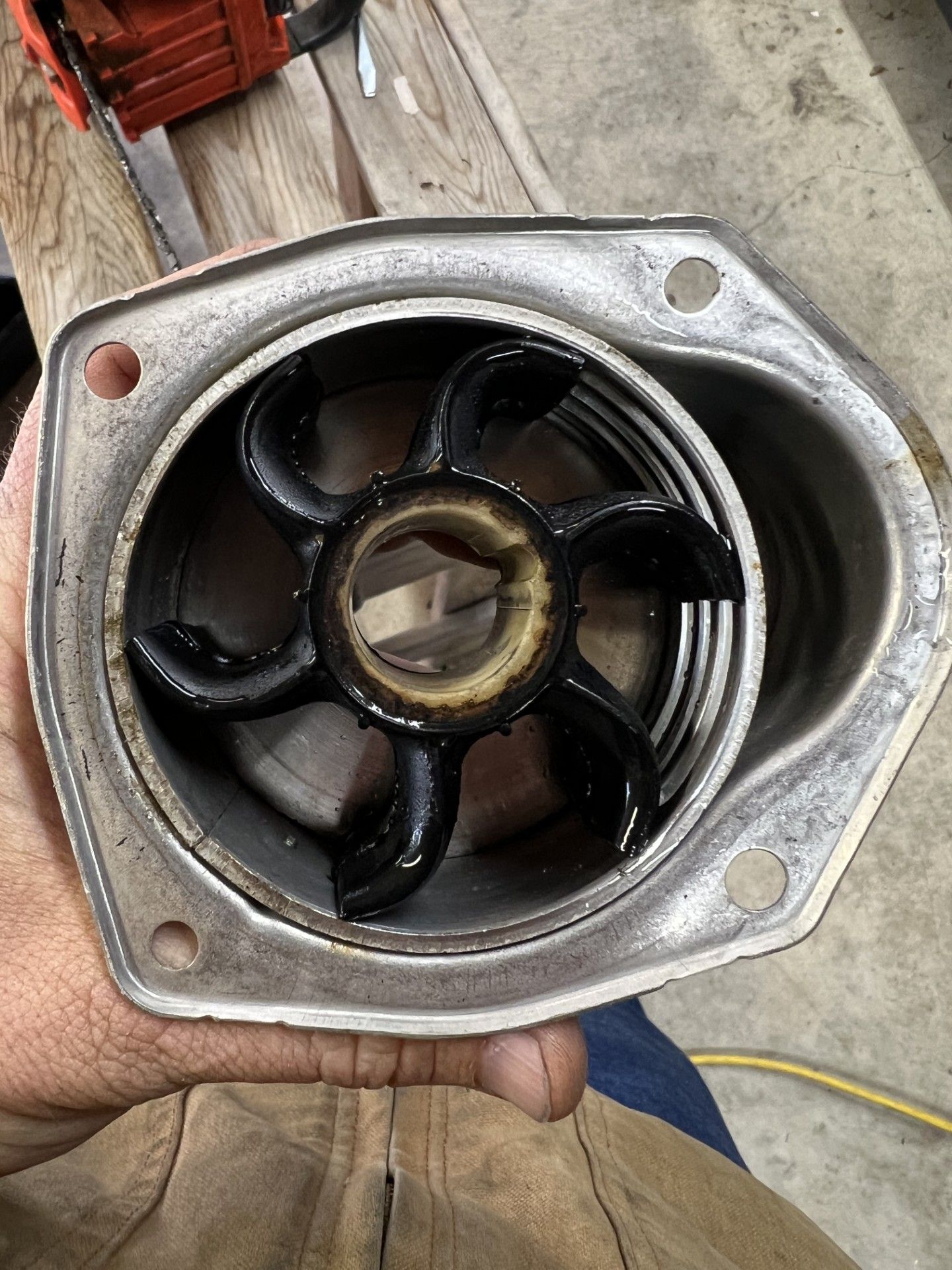 Hand holding a marine water pump housing with a black impeller.