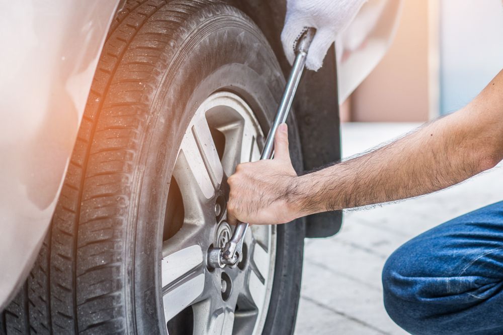 A Man is Changing a Tire on a Car With a Wrench — Turbo's Tyres Pty Ltd In Humpty Doo, NT