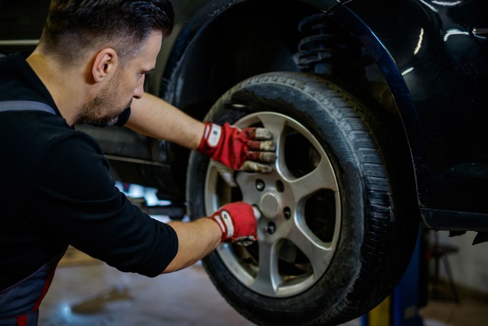 A Man is Changing a Tire on a Car in a Garage — Turbo's Tyres Pty Ltd In Palmerston, NT