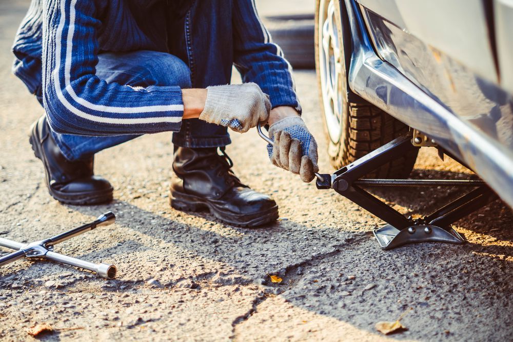 A Man is Changing a Tire on a Car With a Jack — Turbo's Tyres Pty Ltd In Humpty Doo, NT