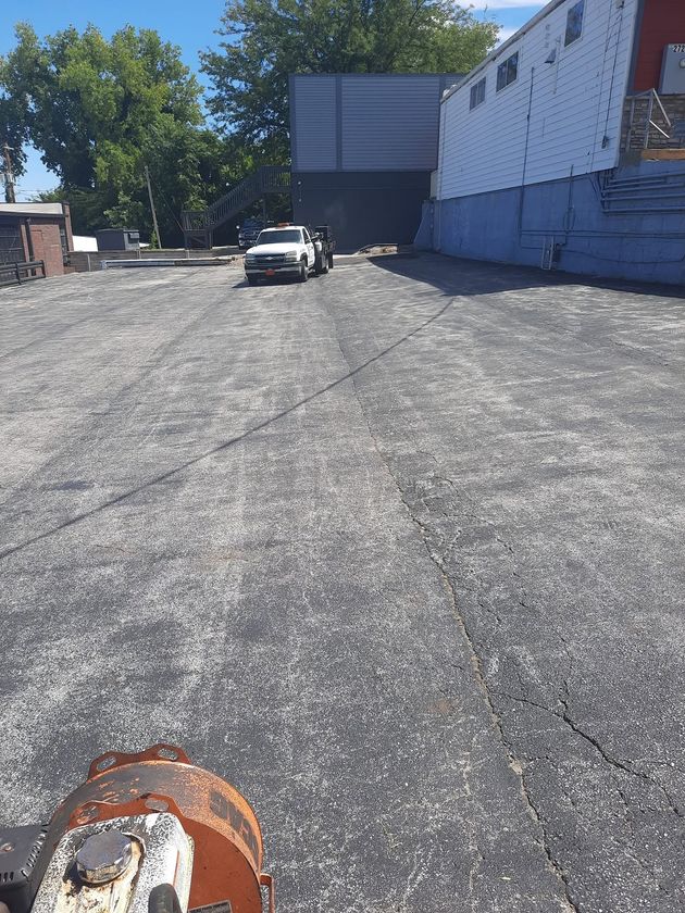 Gravel parking lot beside a blue building, with a parked car in the distance and trees along the edge.