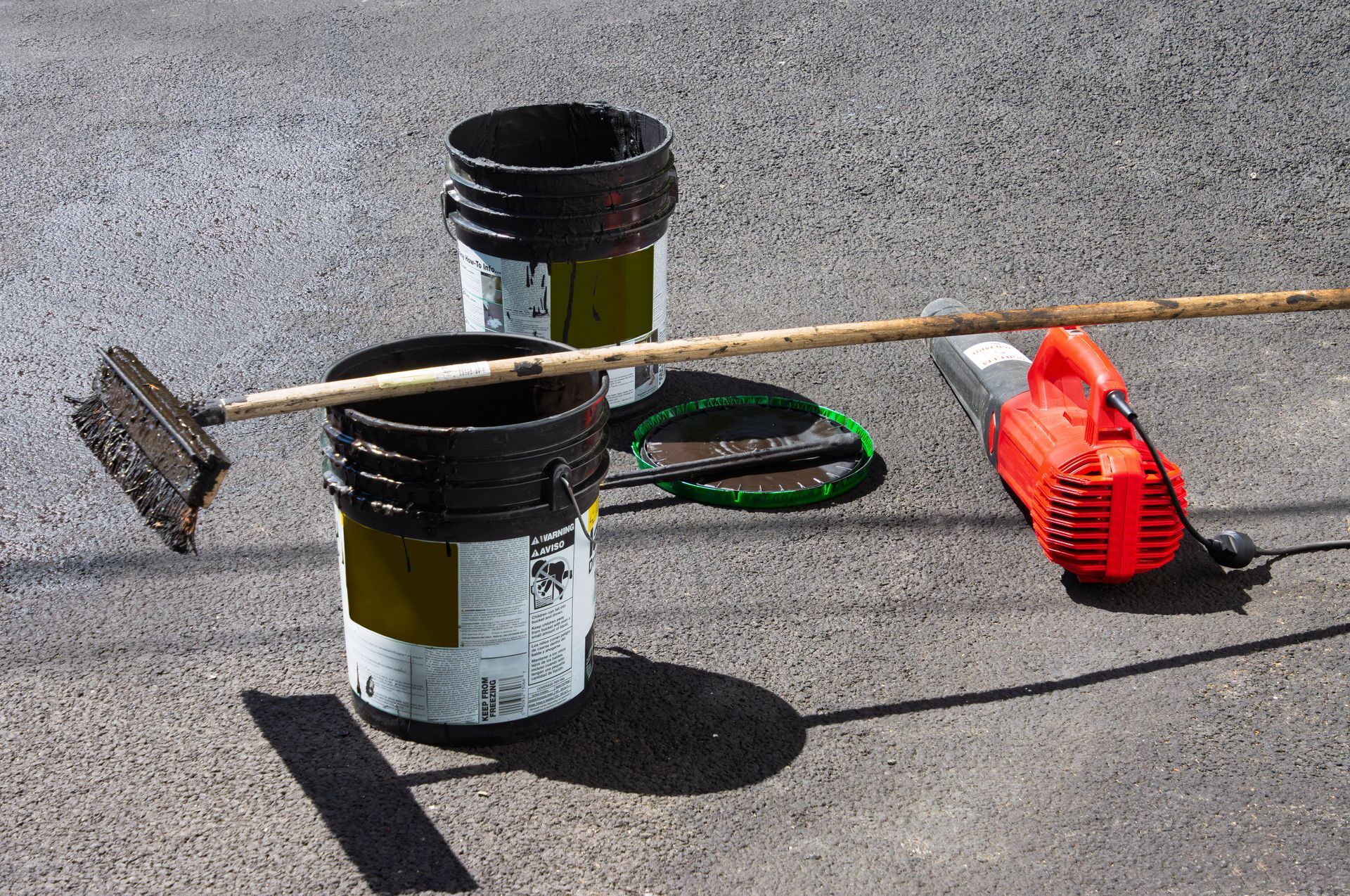 Rooftop vent pipe with brush, coiled hose, and red tool on a flat gravel surface.