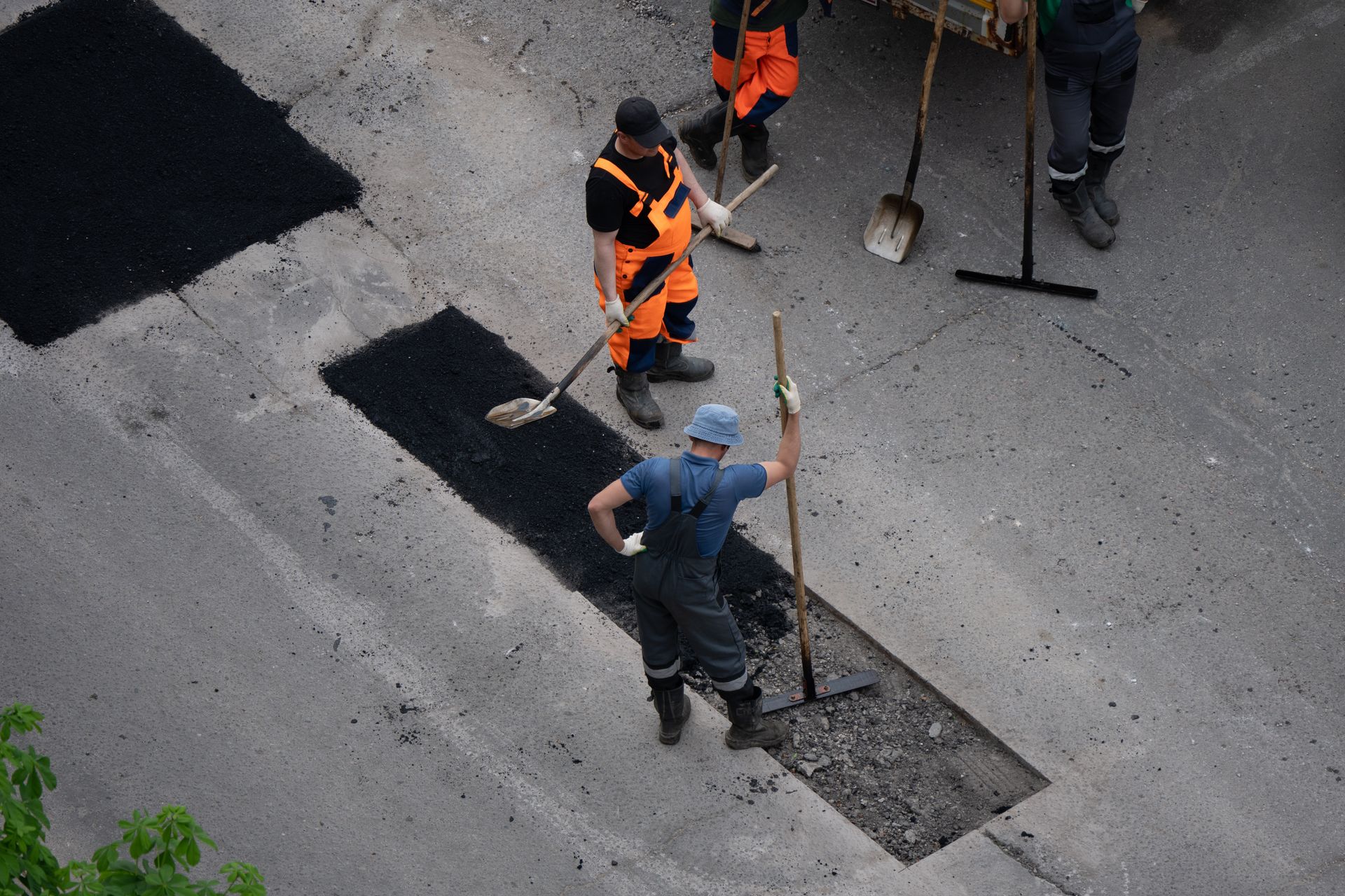 Workers patching potholes on a gray asphalt road, with shovels and fresh black asphalt.