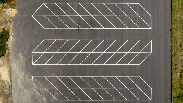 Three empty parking spaces marked with white diagonal lines on gray pavement, viewed from above