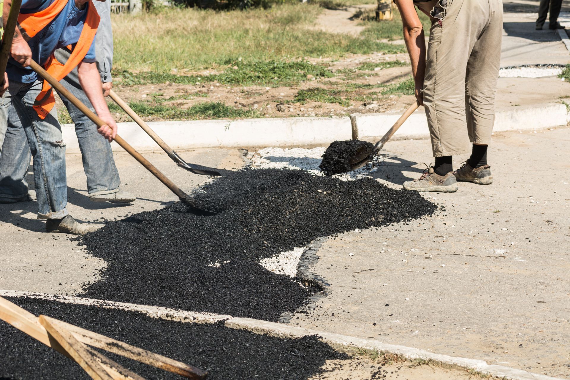 Workers shoveling fresh asphalt to repair a street pothole beside a curb