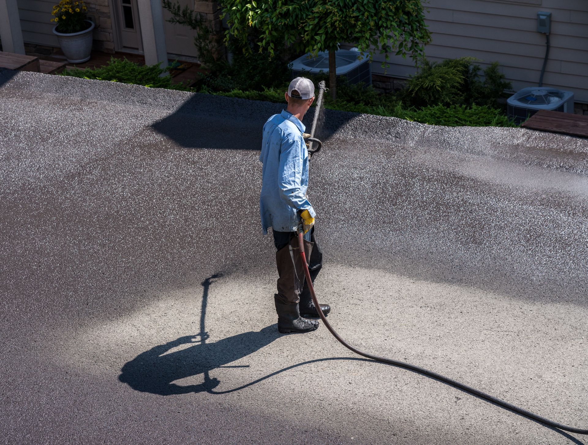 Worker using a power washer on a driveway next to a house