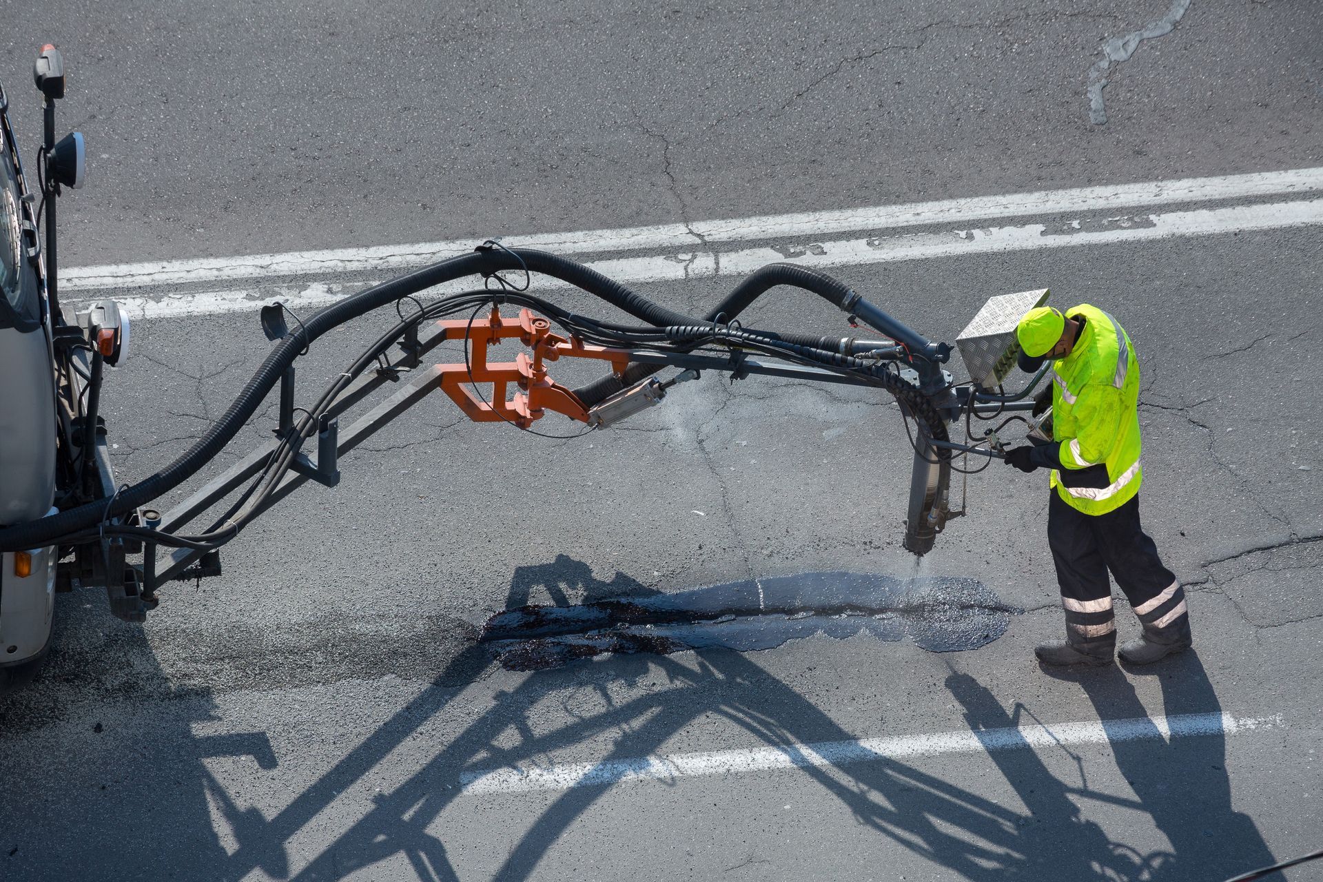 Worker in neon safety gear operating a road-marking machine on pavement.