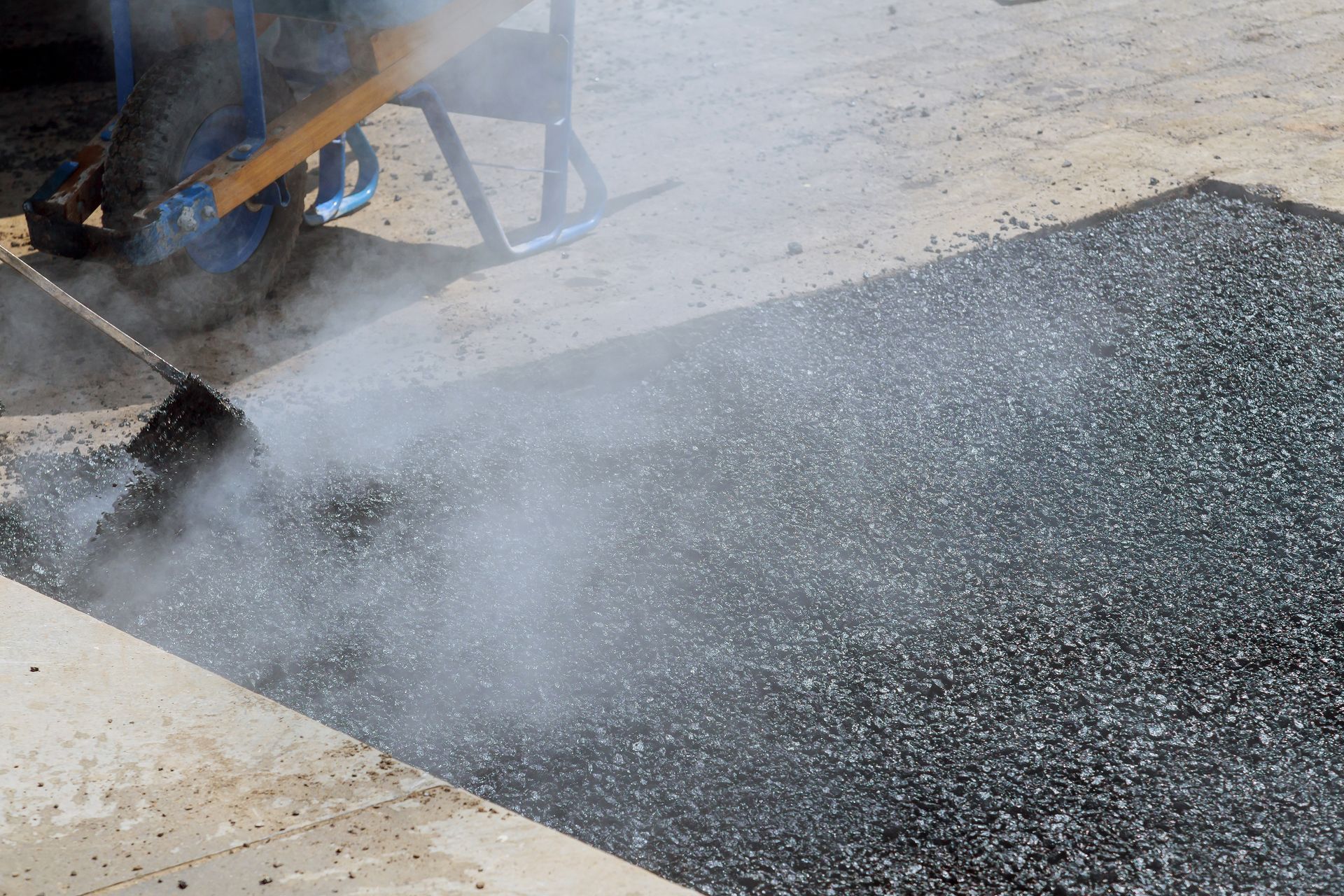 Asphalt paving machine spraying hot tar onto a road surface, creating black pavement and steam