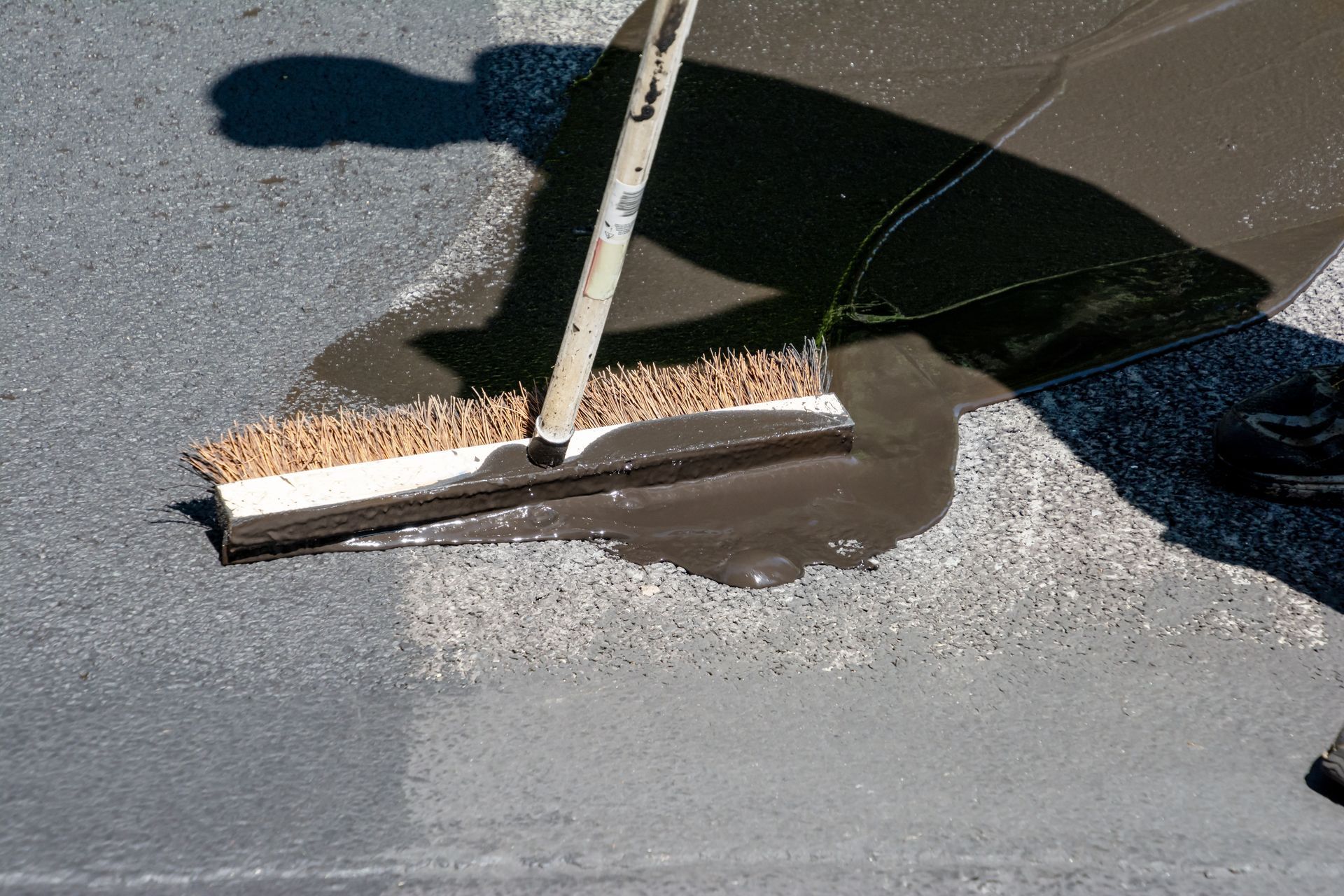 Worker using a squeegee to spread wet material on pavement beside a curb barrier