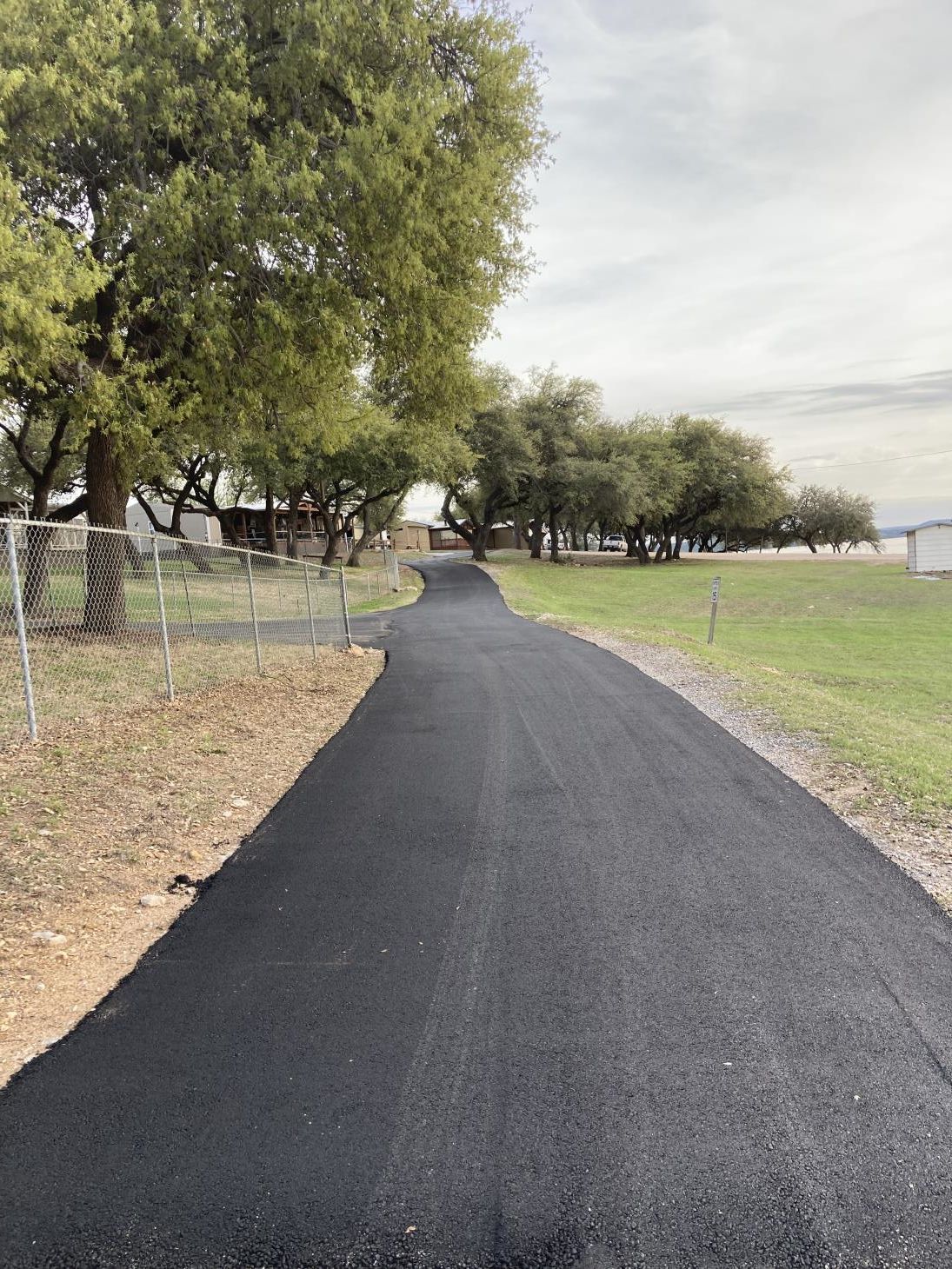 An asphalt roadway stretching into the distance, lined with white lane markings and bordered by green trees on either side.