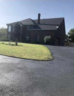 A person applies a layer of sealcoating to an asphalt driveway, ensuring its protection and longevity.