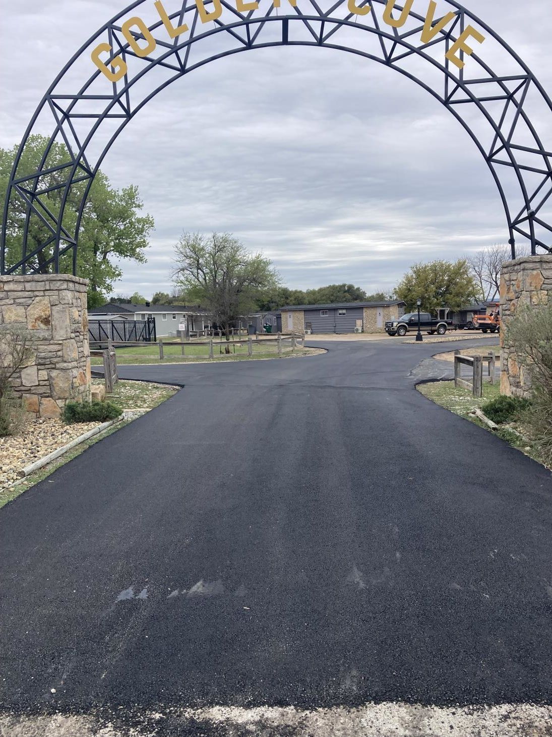 Person applying driveway sealer with a brush to protect and enhance the surface of the asphalt.