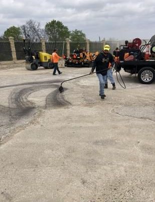 A worker in a yellow vest is laying asphalt to repair a road under the bright rays of the sun.