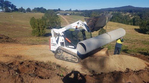 White Excavator Lifting Pipe — Earthmoving Services  in Eungai Creek, NSW