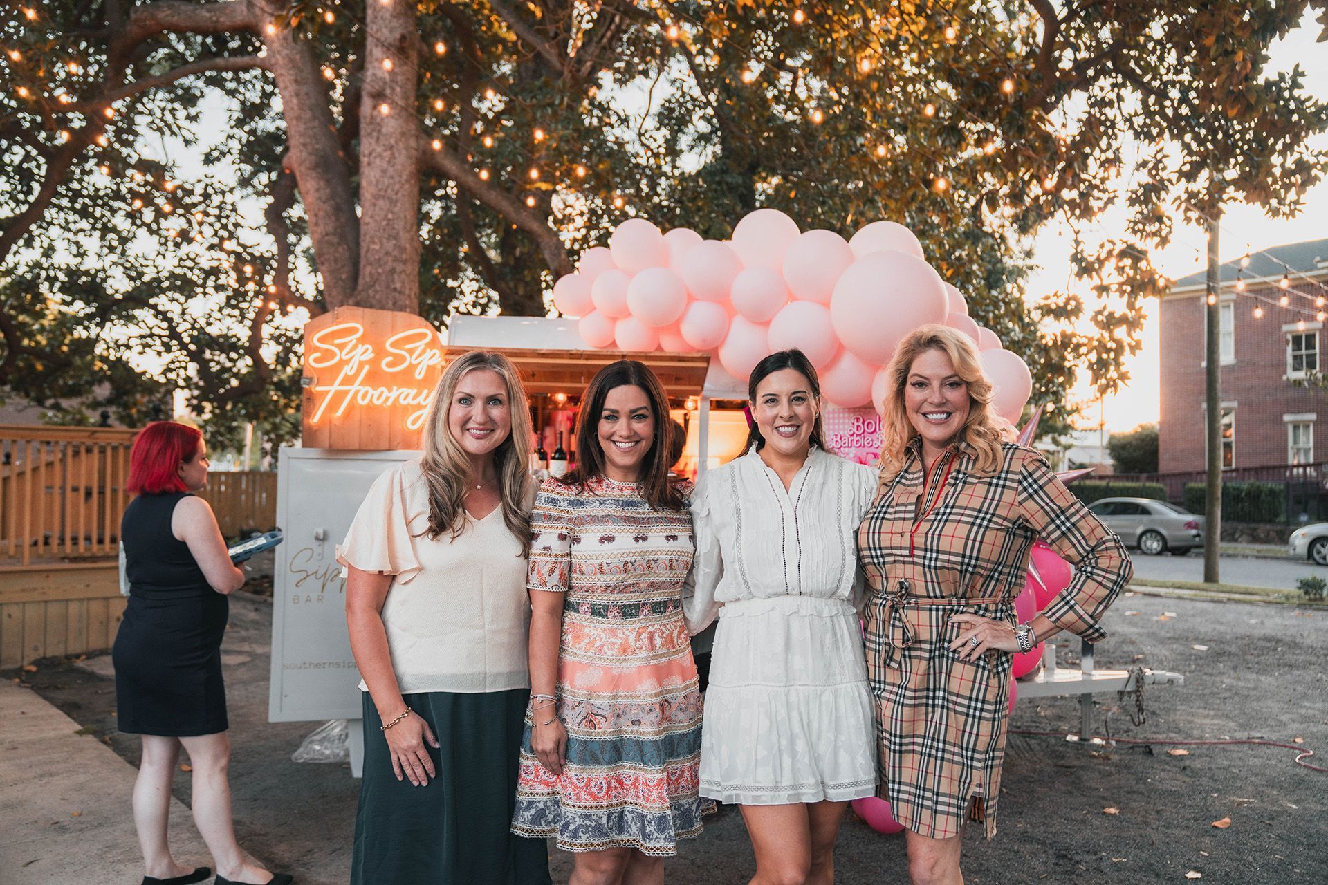 A group of women are posing for a picture in front of a food truck filled with pink balloons.