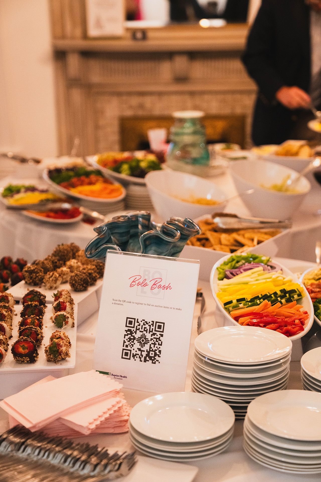 A buffet table with plates , bowls , and a sign on it.