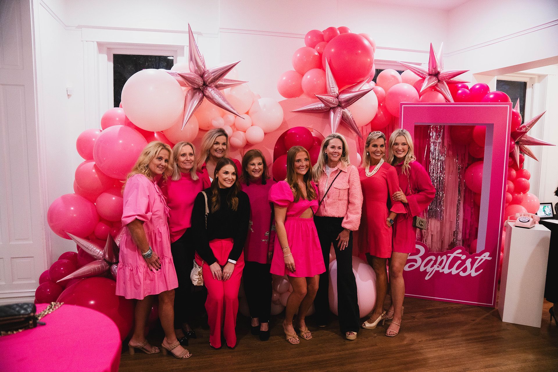 A group of women are posing for a picture in front of a wall of pink balloons.