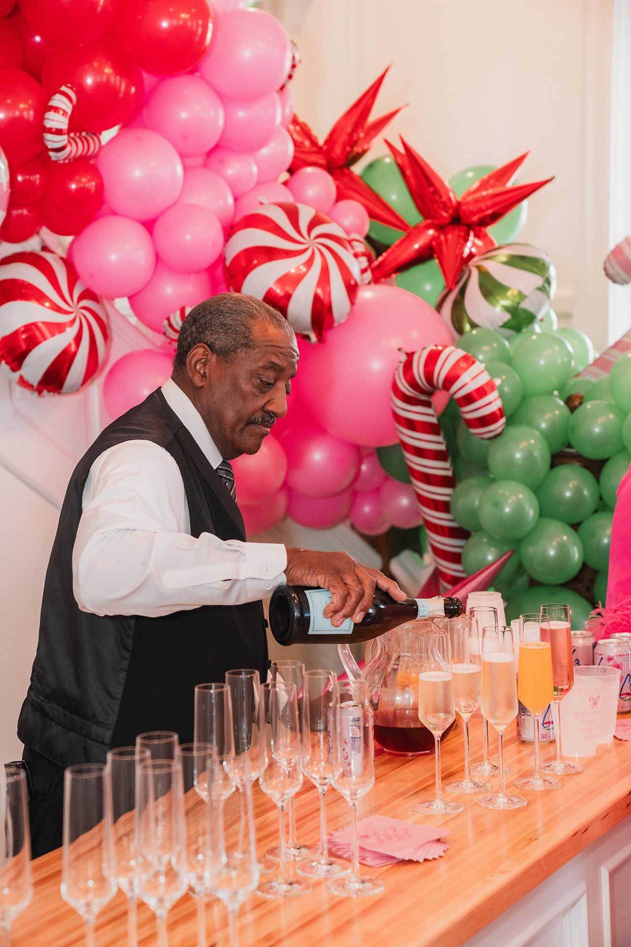 A man is pouring wine into a bar with balloons in the background.