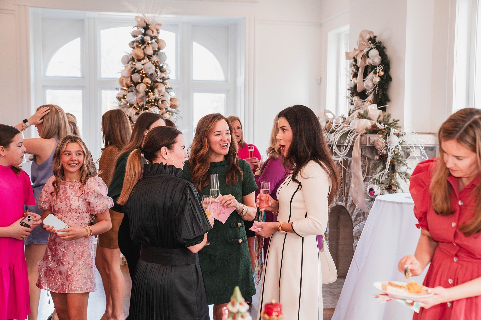 A group of women are standing in a room with Christmas trees at E.O. Manees House