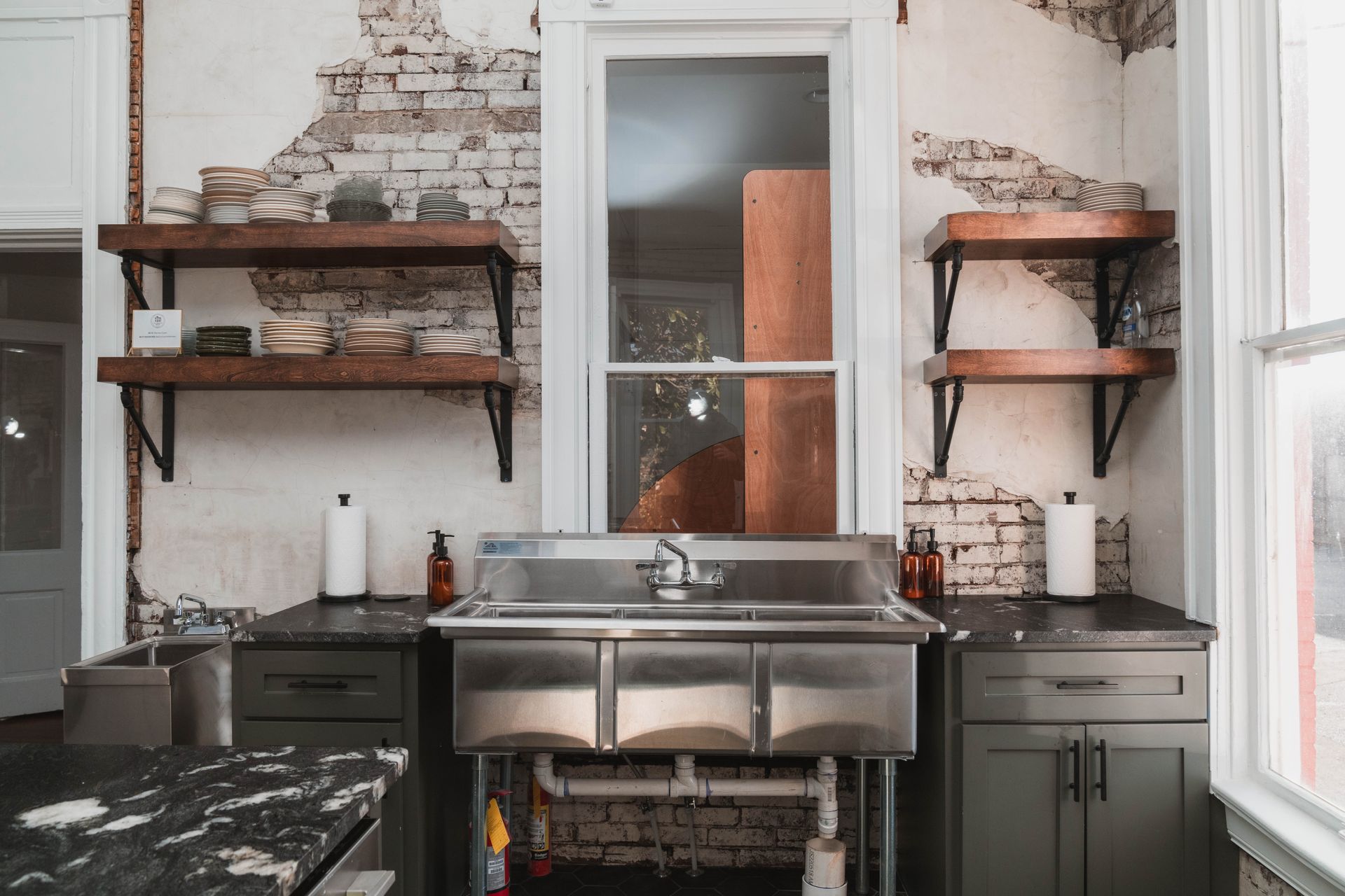 A kitchen with a sink , cabinets , shelves and a window.
