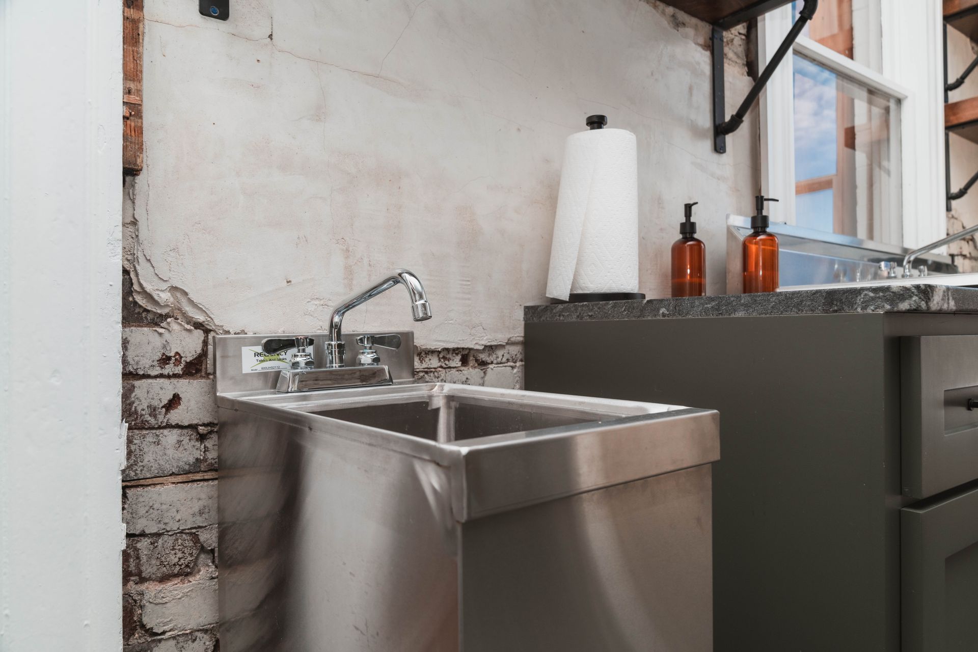 A stainless steel sink in a kitchen next to a brick wall.