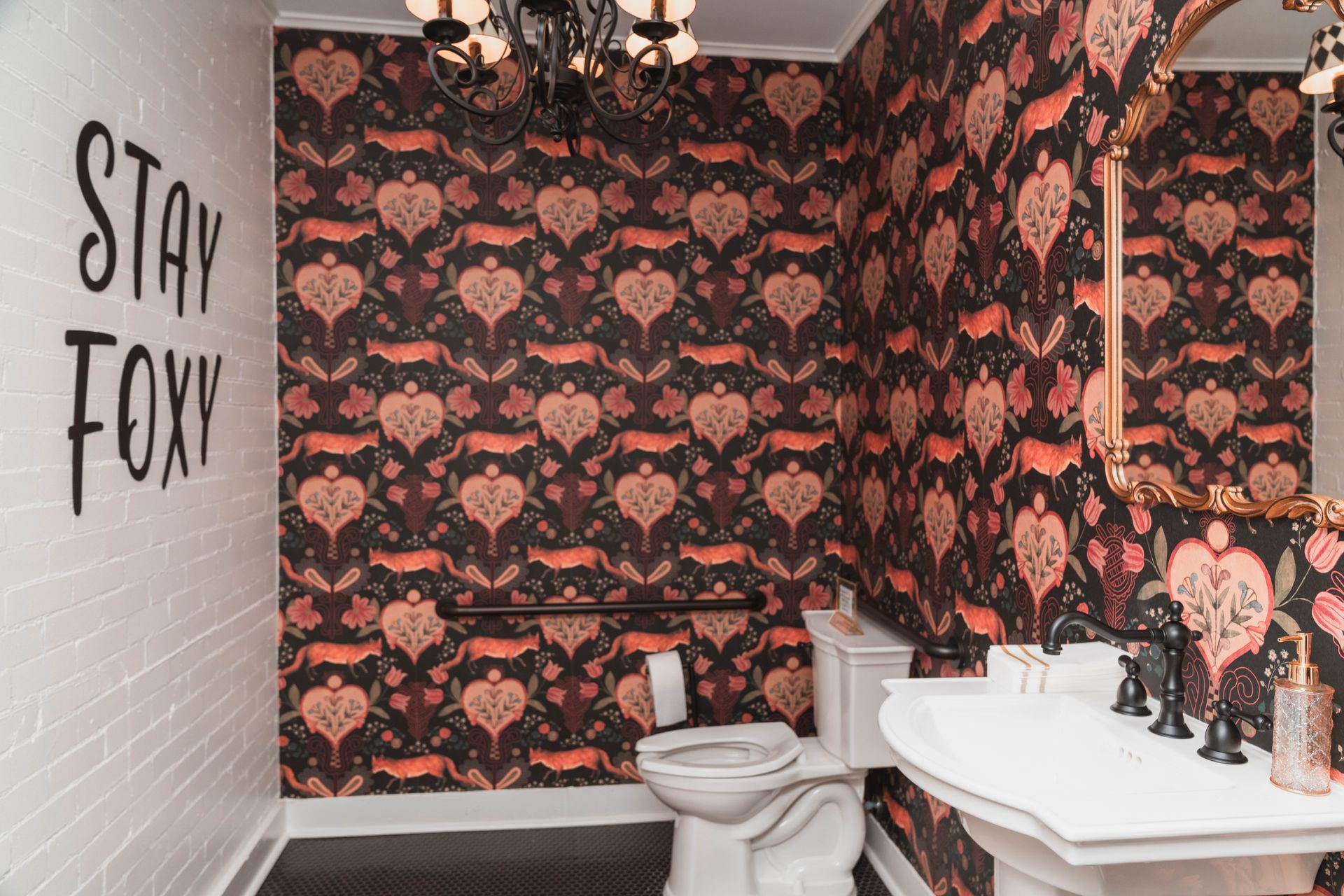 A bathroom with a toilet , sink , mirror and wallpaper that says stay foxy.