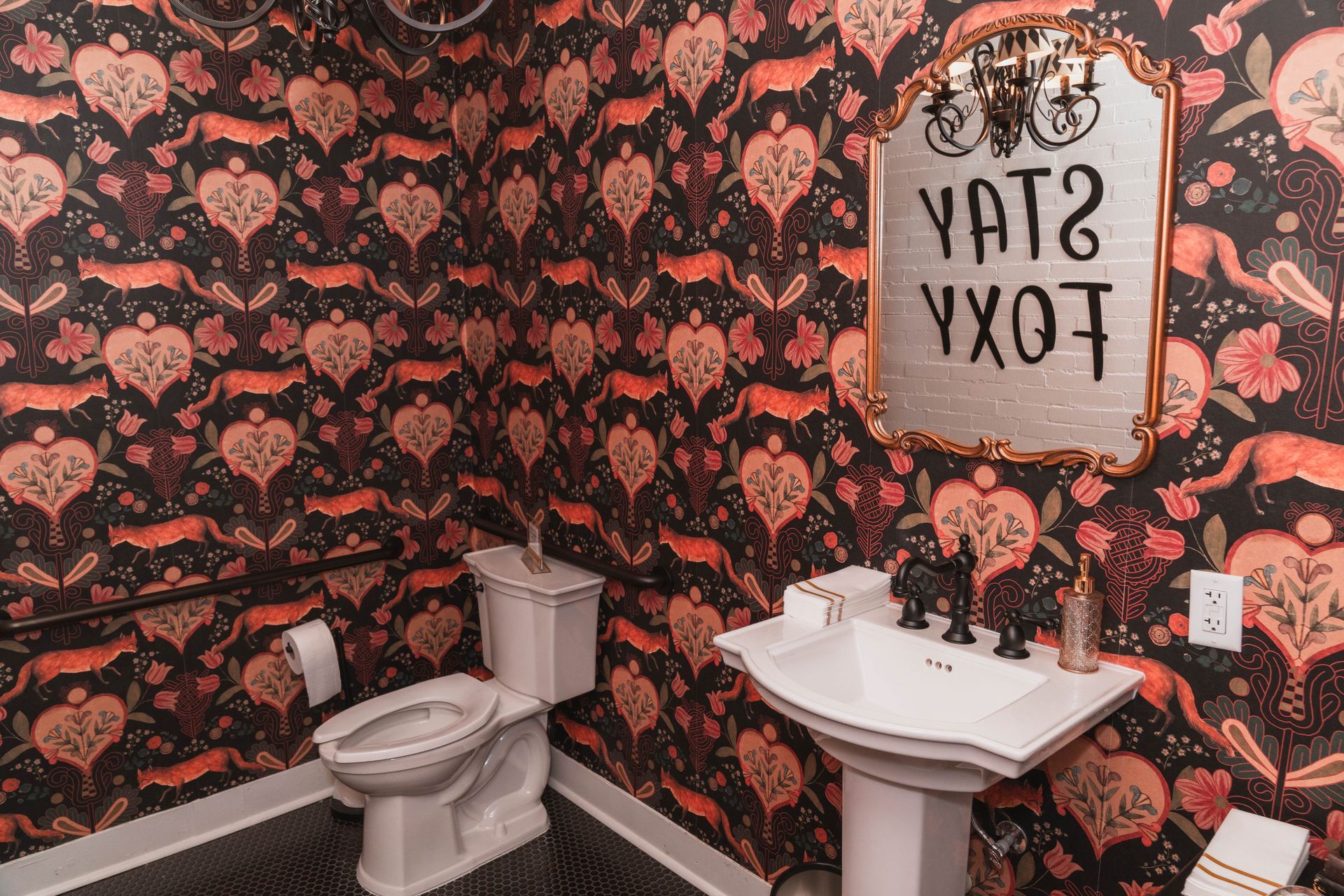A bathroom with a toilet , sink , mirror and wallpaper.