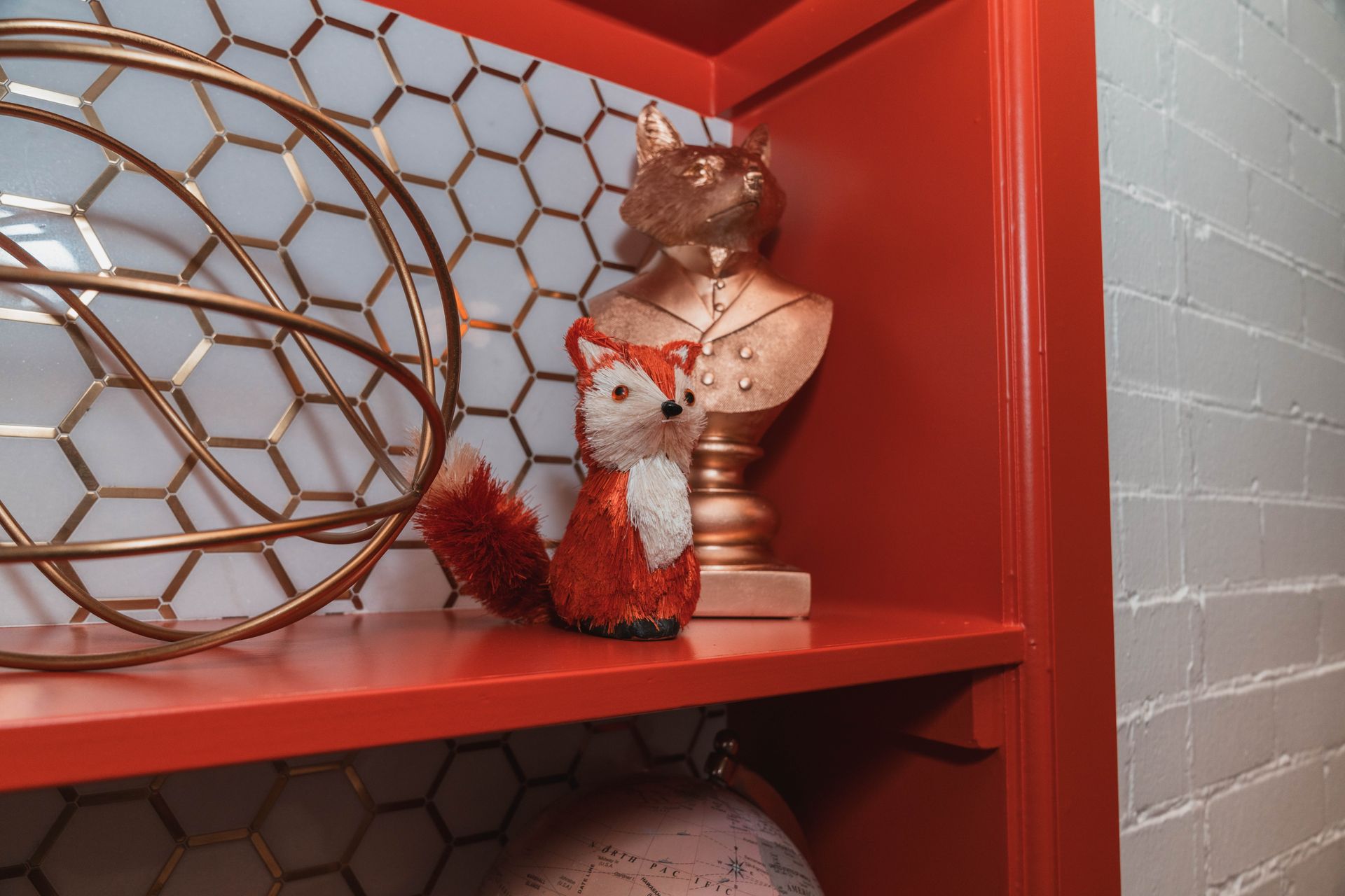 A stuffed fox is sitting on a red shelf next to a statue of a fox.
