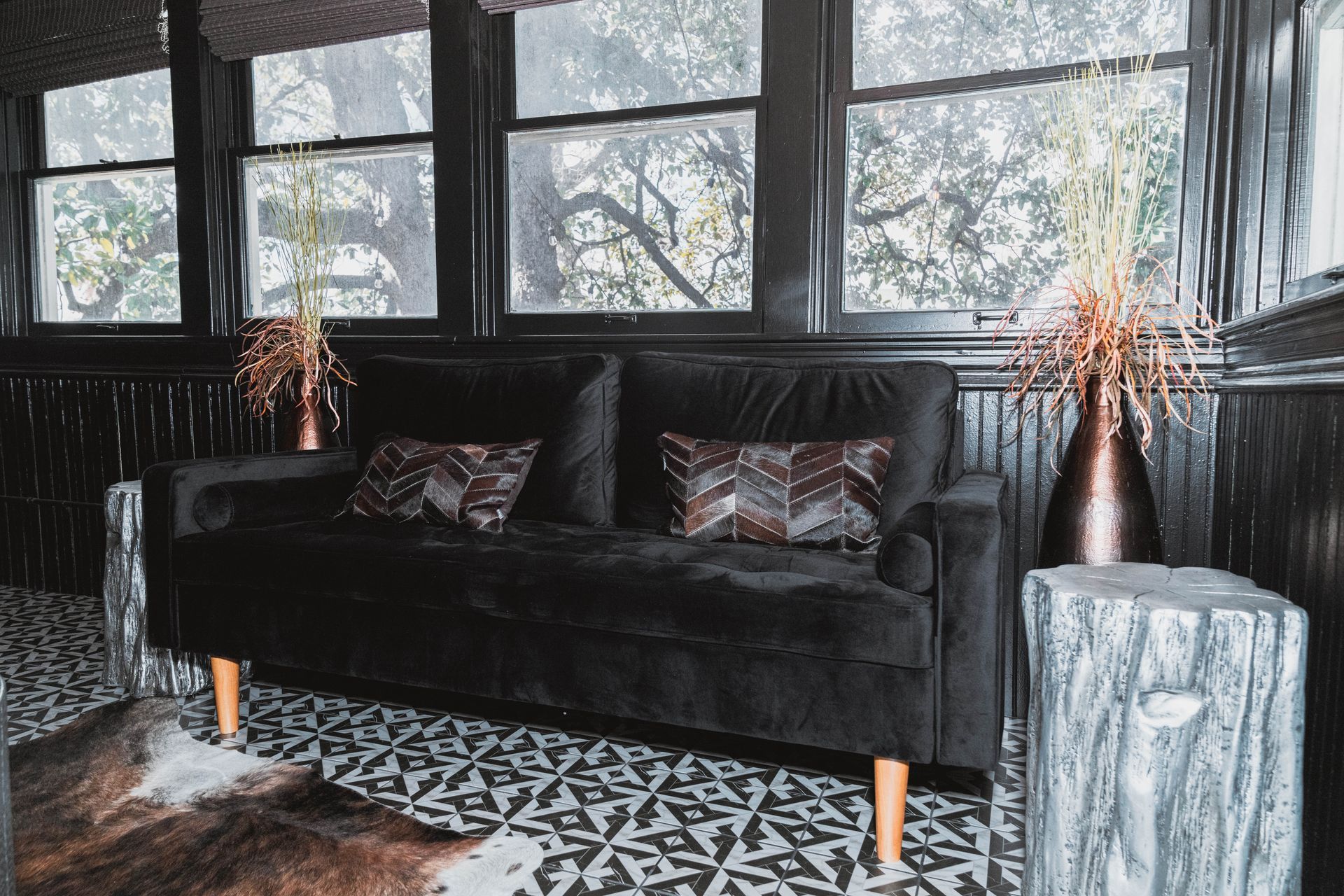 A black couch is sitting in a living room next to a window.