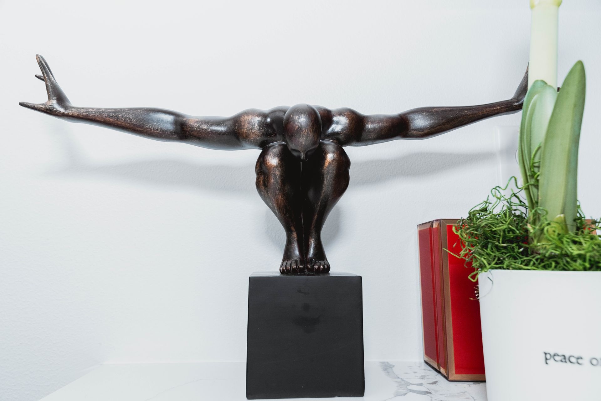 A statue of a man with his arms outstretched is sitting on a table next to a potted plant.