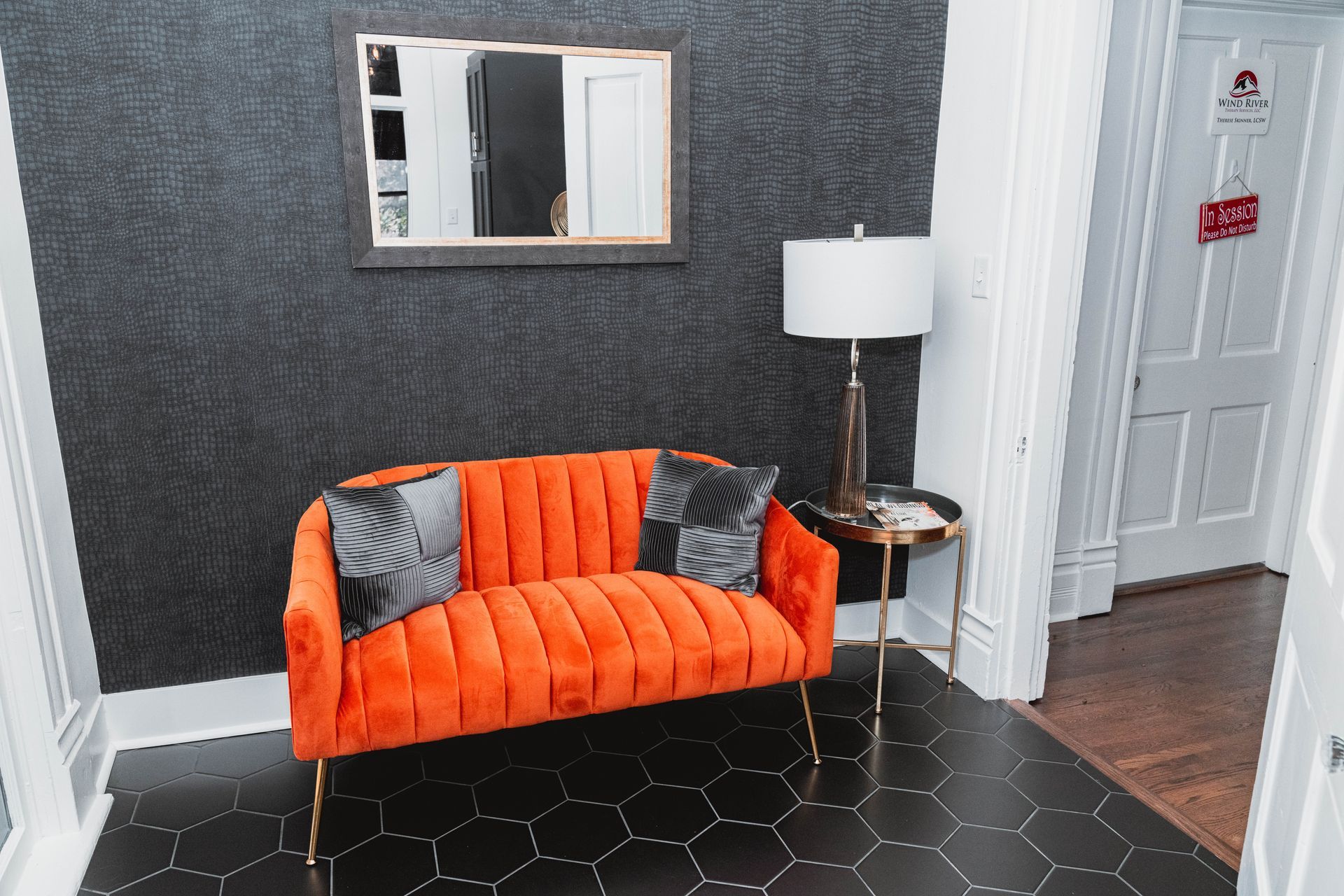 An orange couch is sitting in a waiting room next to a mirror.