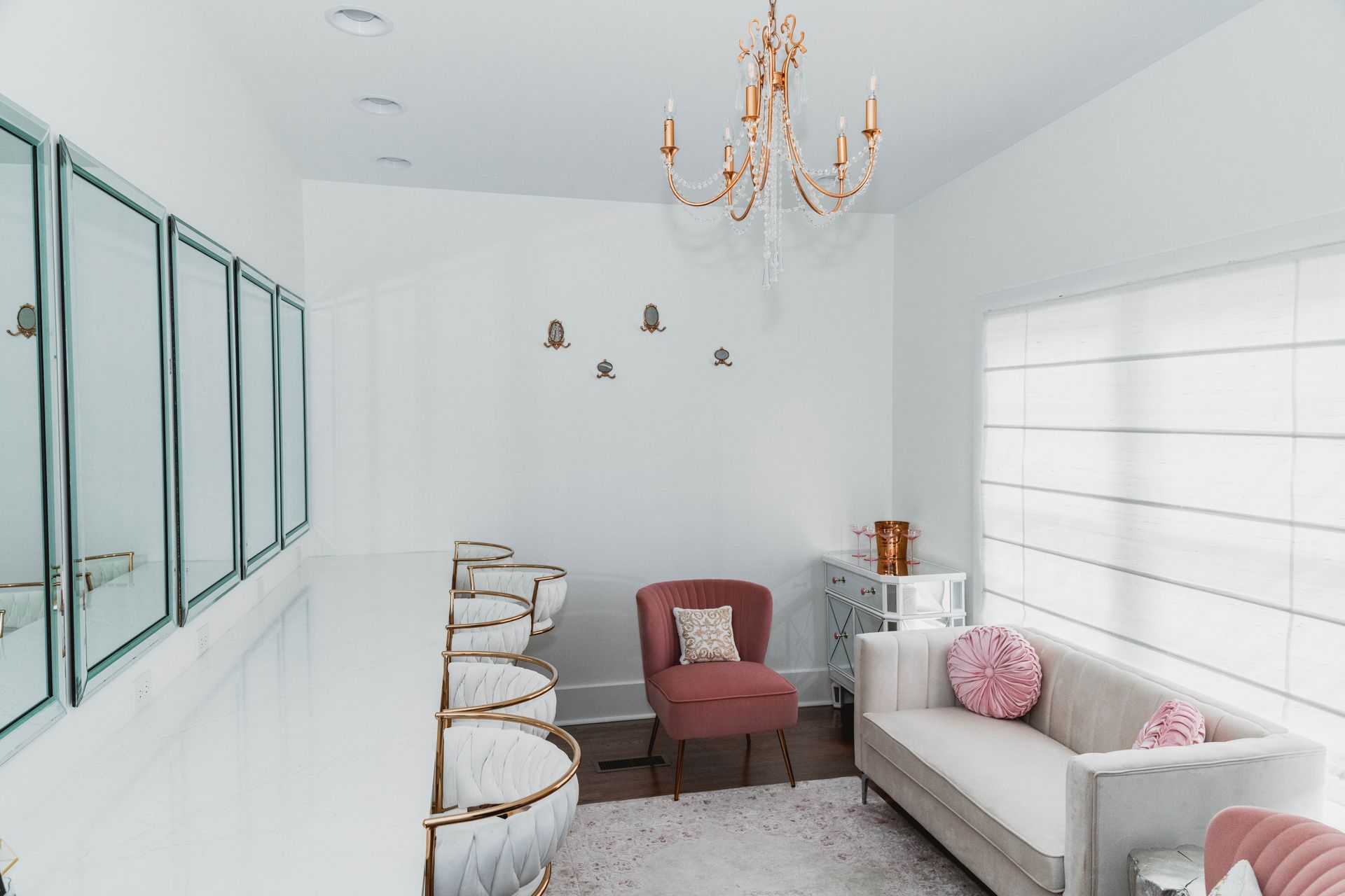 A living room with a couch , chairs , mirrors and a chandelier.