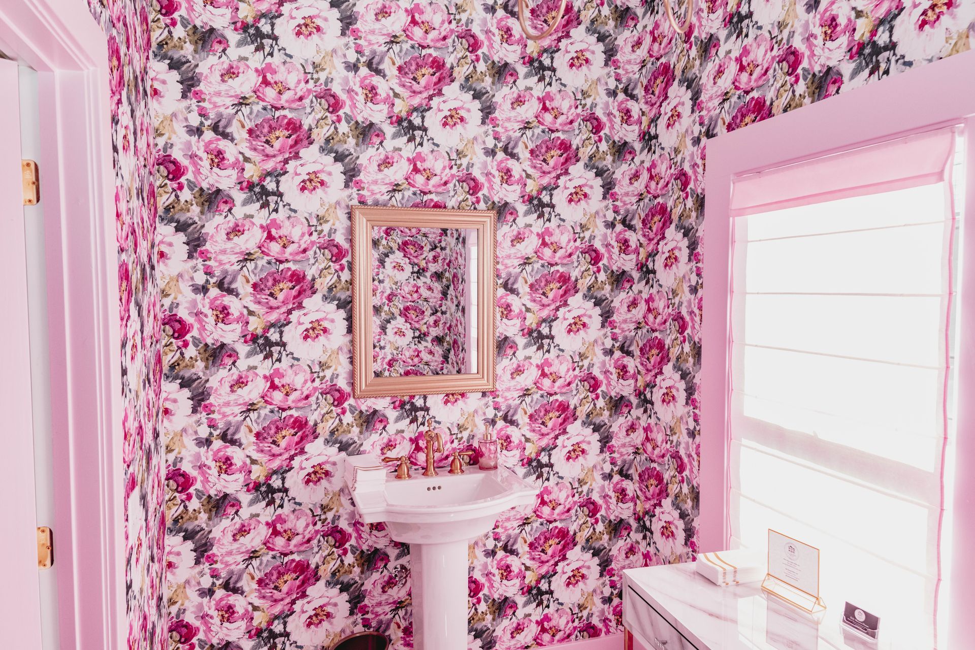 A bathroom with pink floral wallpaper , a sink , and a mirror.
