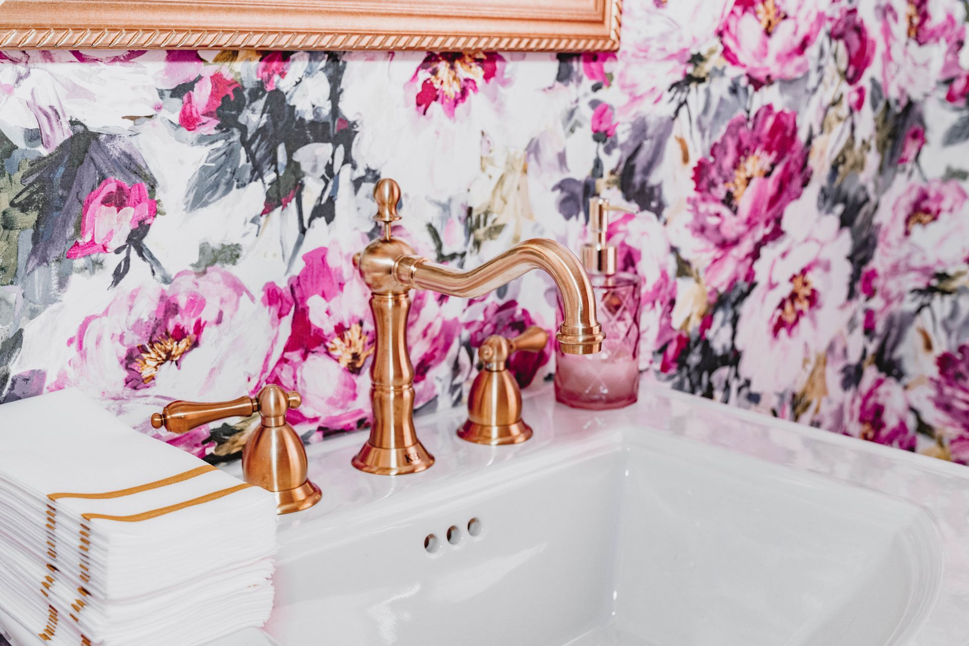 A bathroom with a sink , mirror , and floral wallpaper.