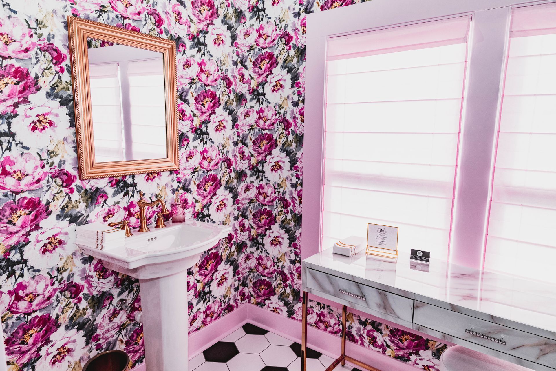 A bathroom with a sink , mirror , and floral wallpaper.