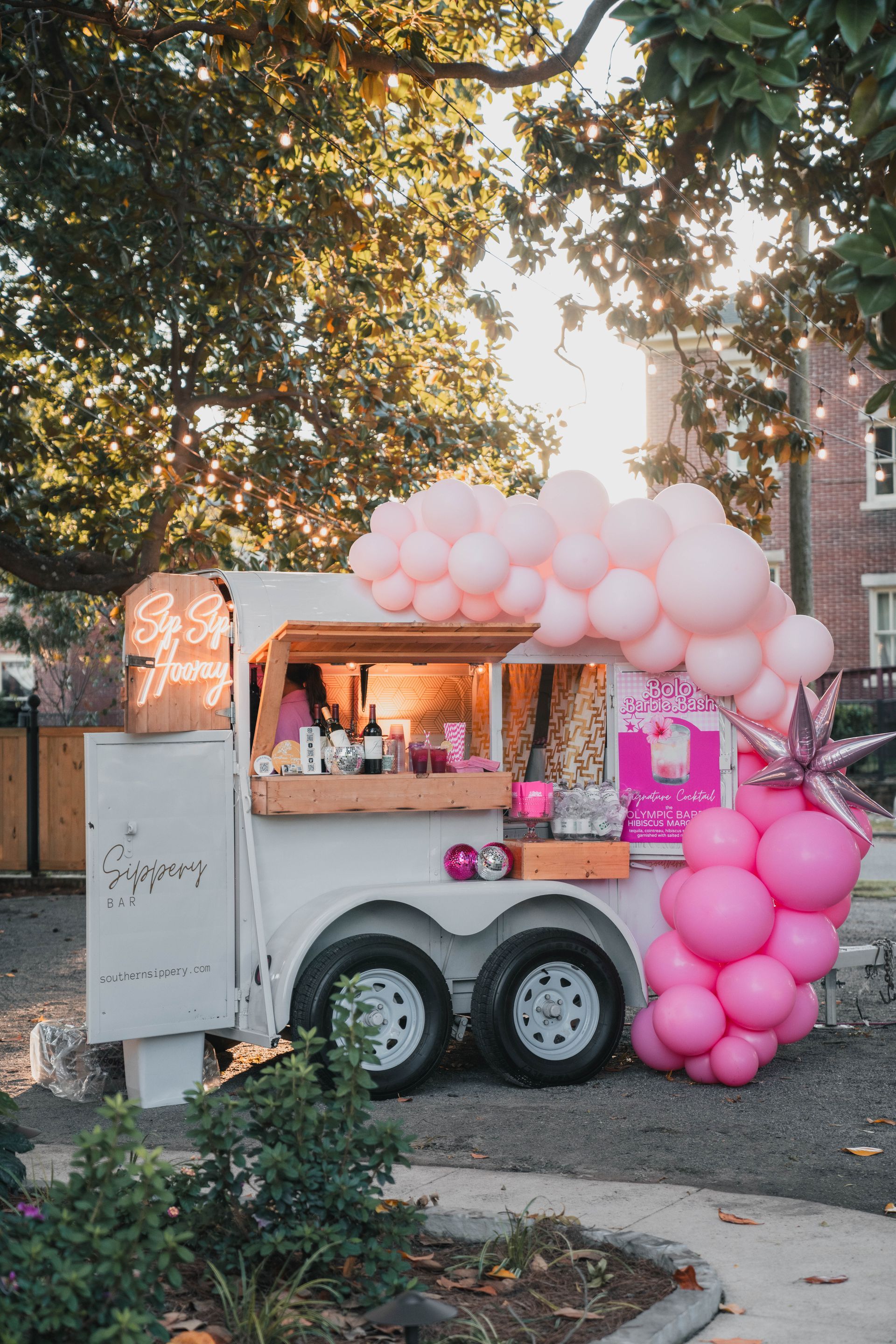A food truck decorated with pink balloons is parked on the side of the road.