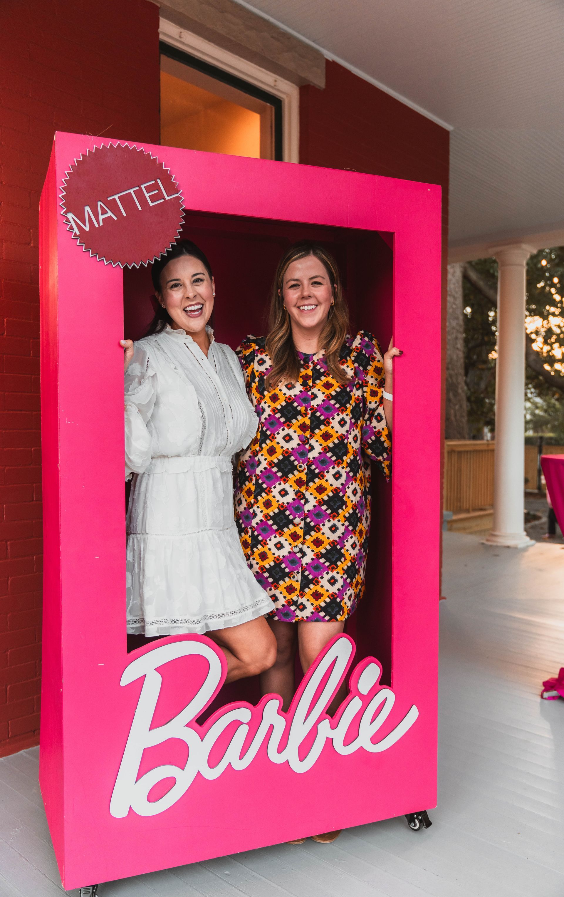 Two women are standing in a pink barbie box.