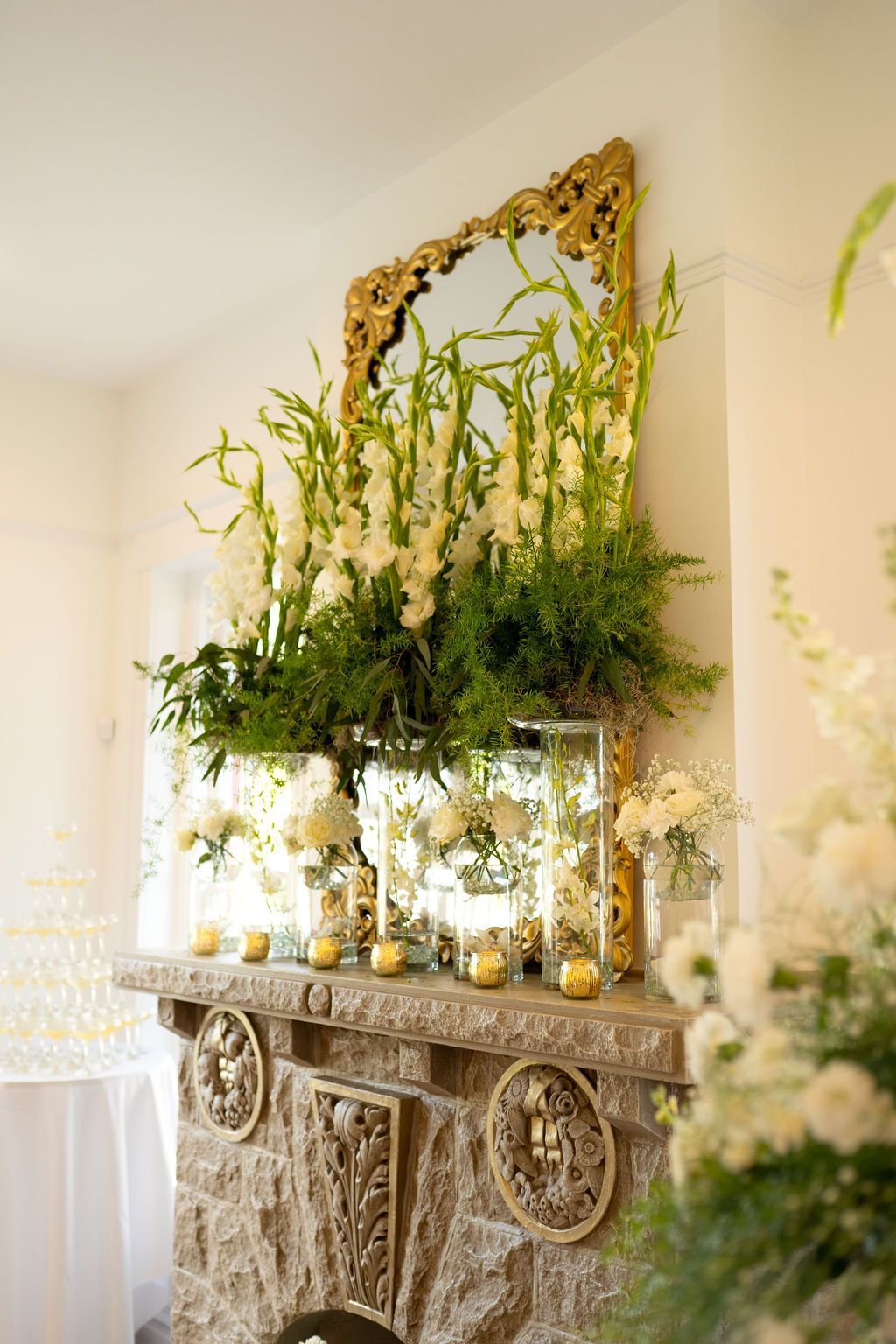 A fireplace with flowers and candles on it and a mirror above it.