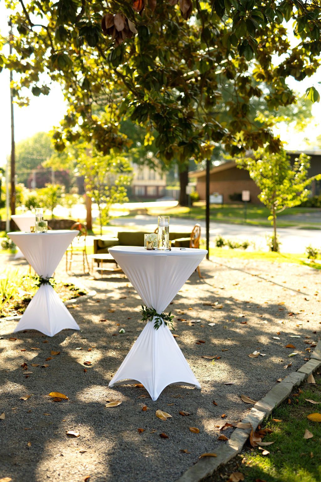 Two white tables are sitting under a tree in a park.