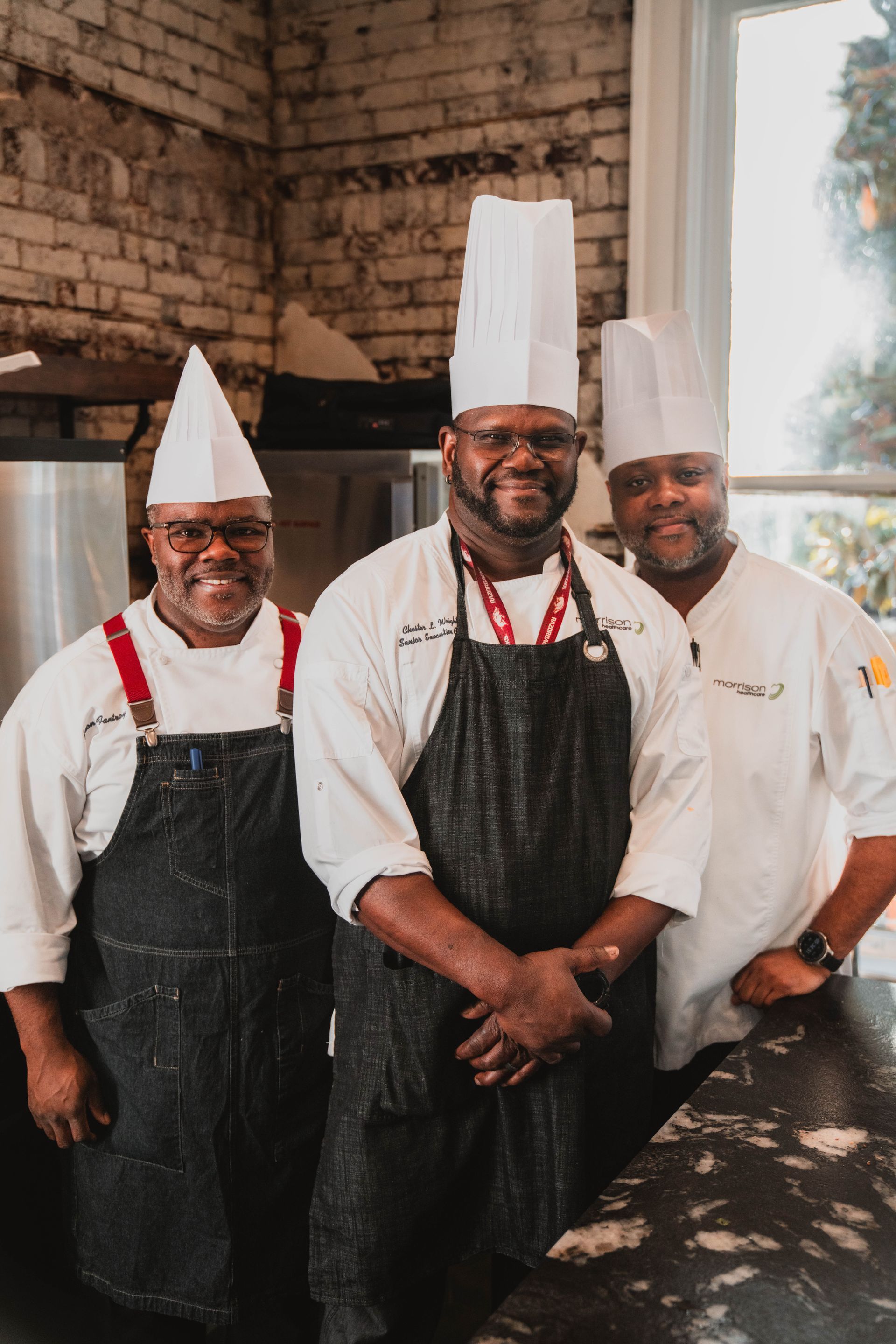 Three chefs are posing for a picture in a kitchen.