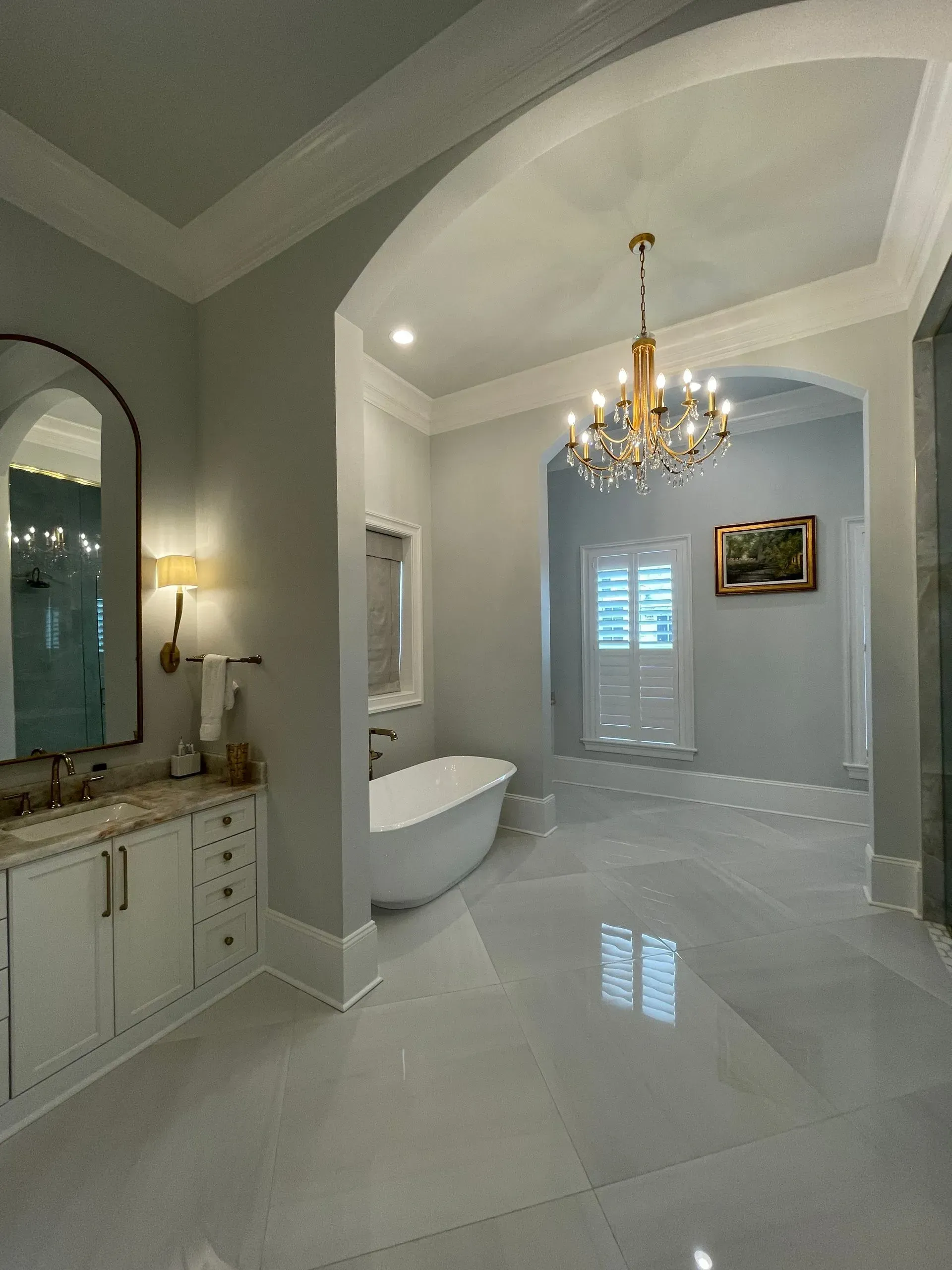 A bathroom with a tub , sink , mirror and chandelier.