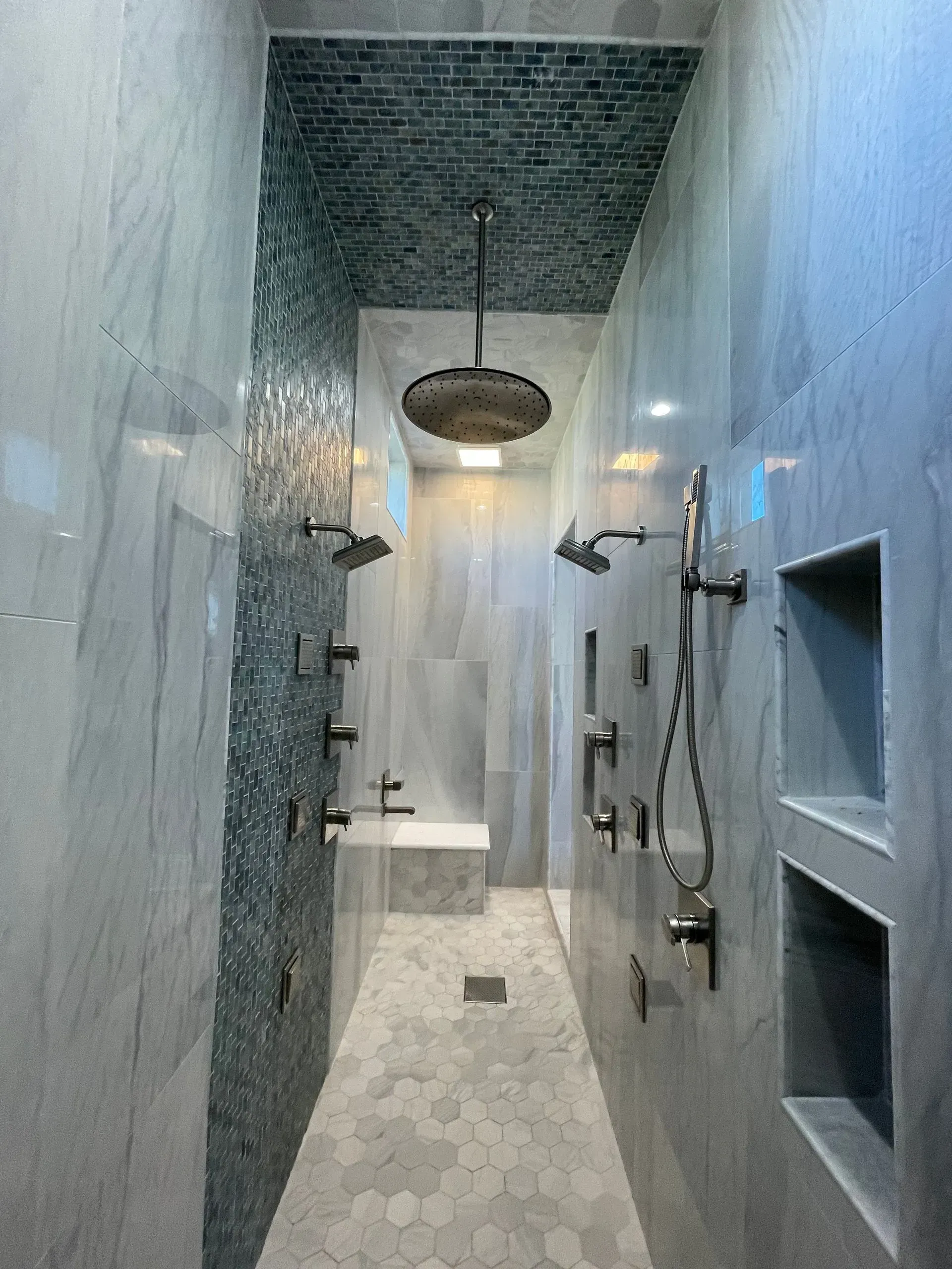 A long shower with a lot of shower heads and a ceiling fan.
