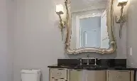 A bathroom with a toilet , sink , mirror and lights.