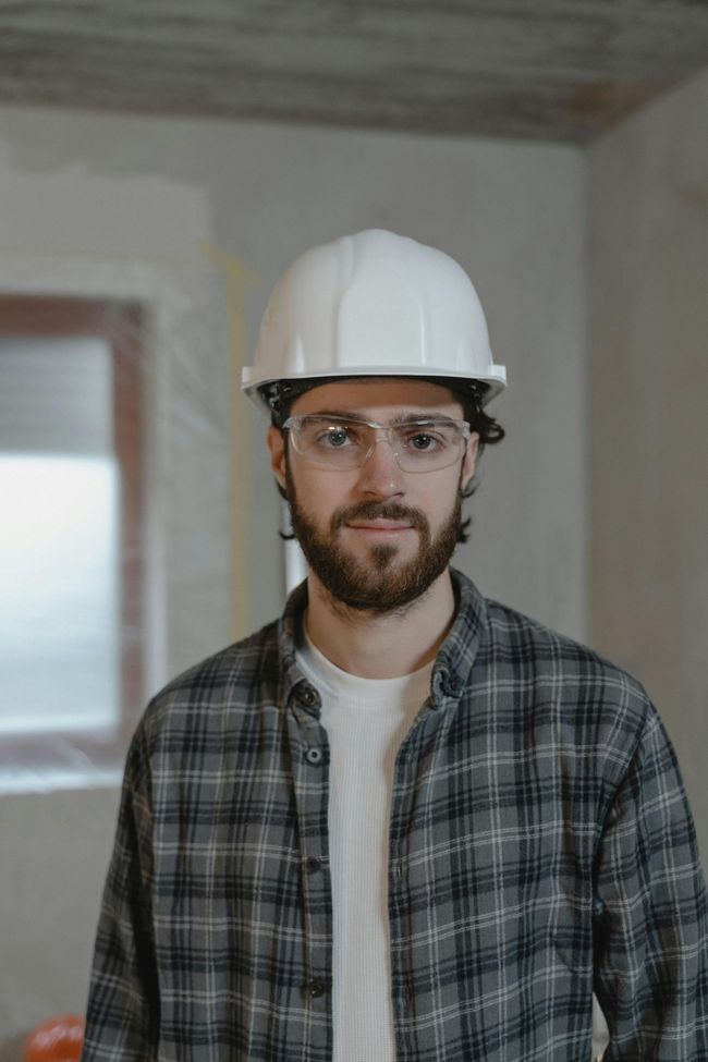 A man wearing a hard hat and goggles is standing in a room.