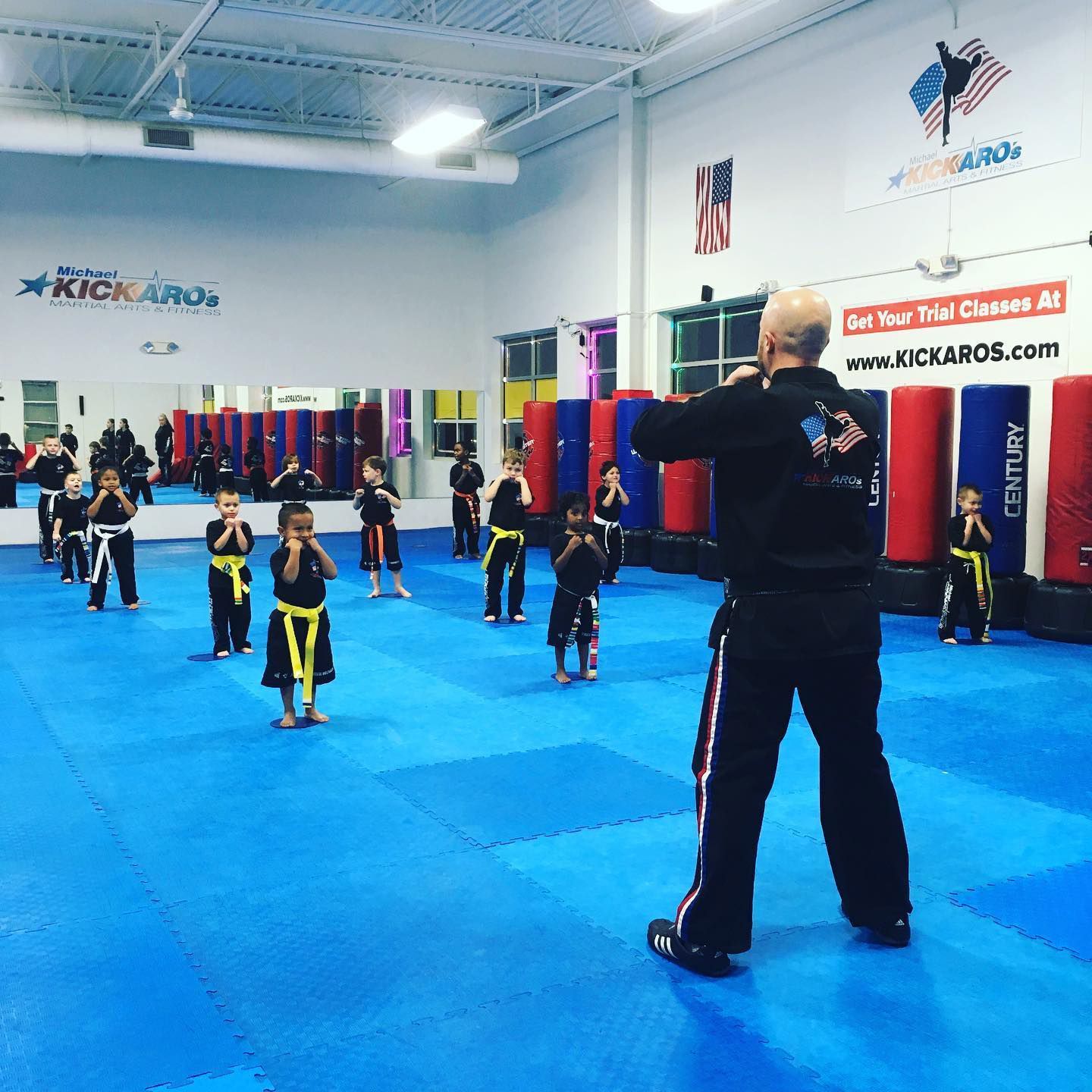 a man stands in front of a group of kids in a martial arts gym