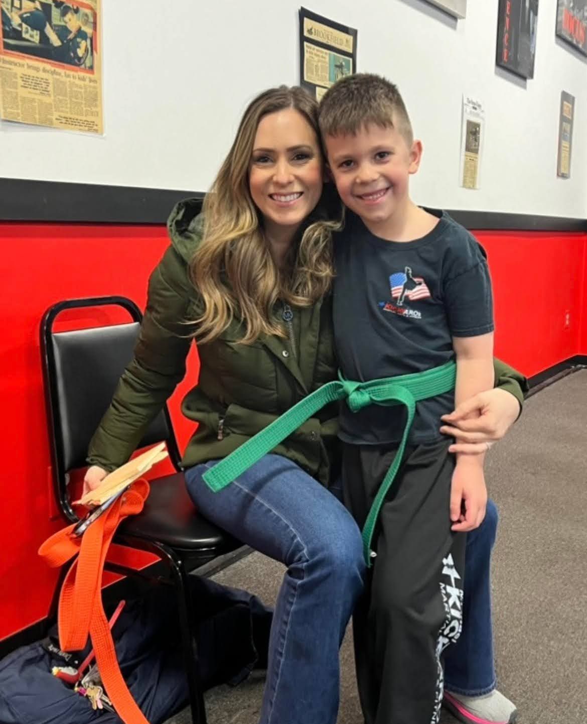 A woman is sitting next to a boy with a green belt.