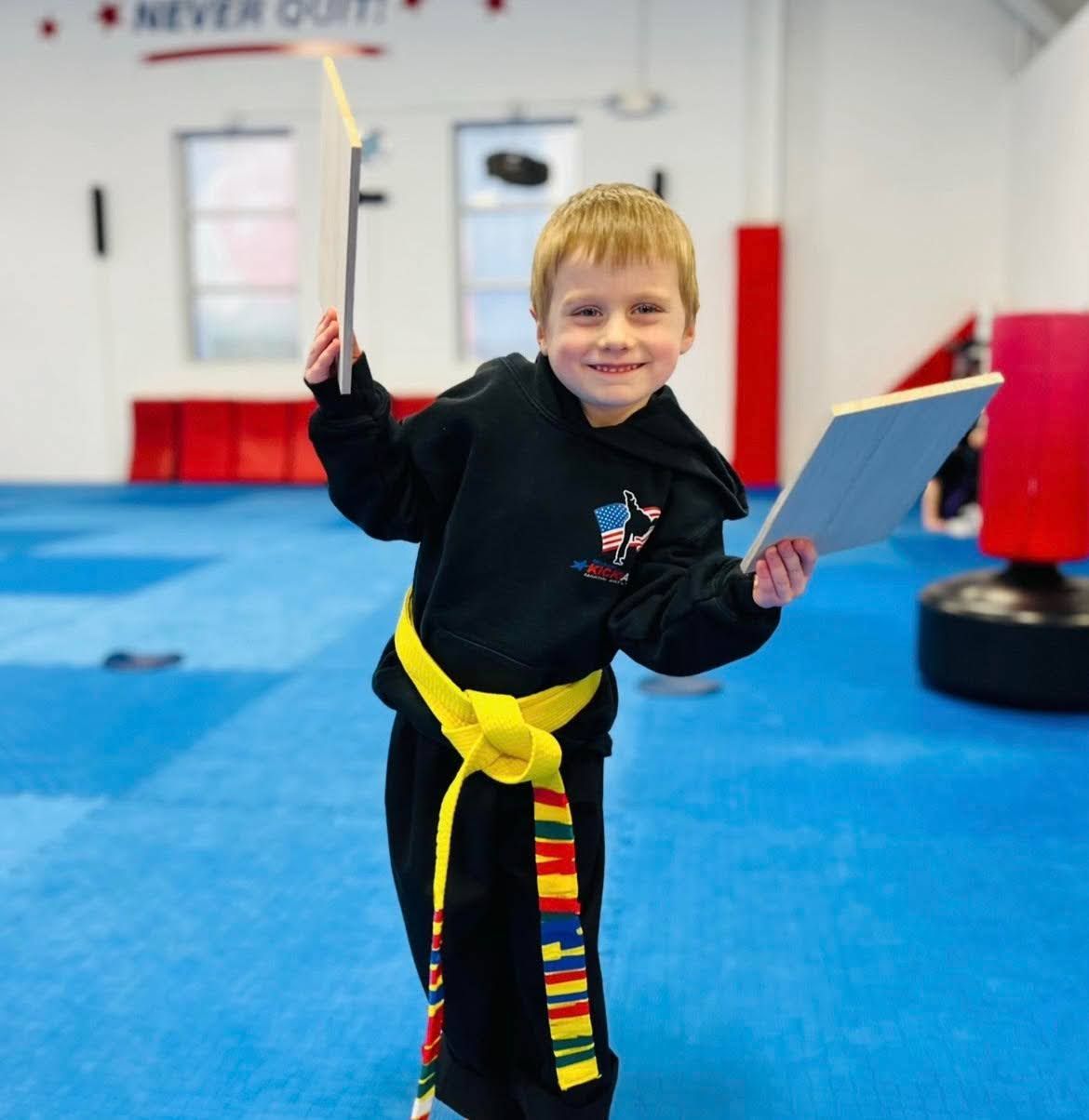 A young boy with a yellow belt holds a tablet