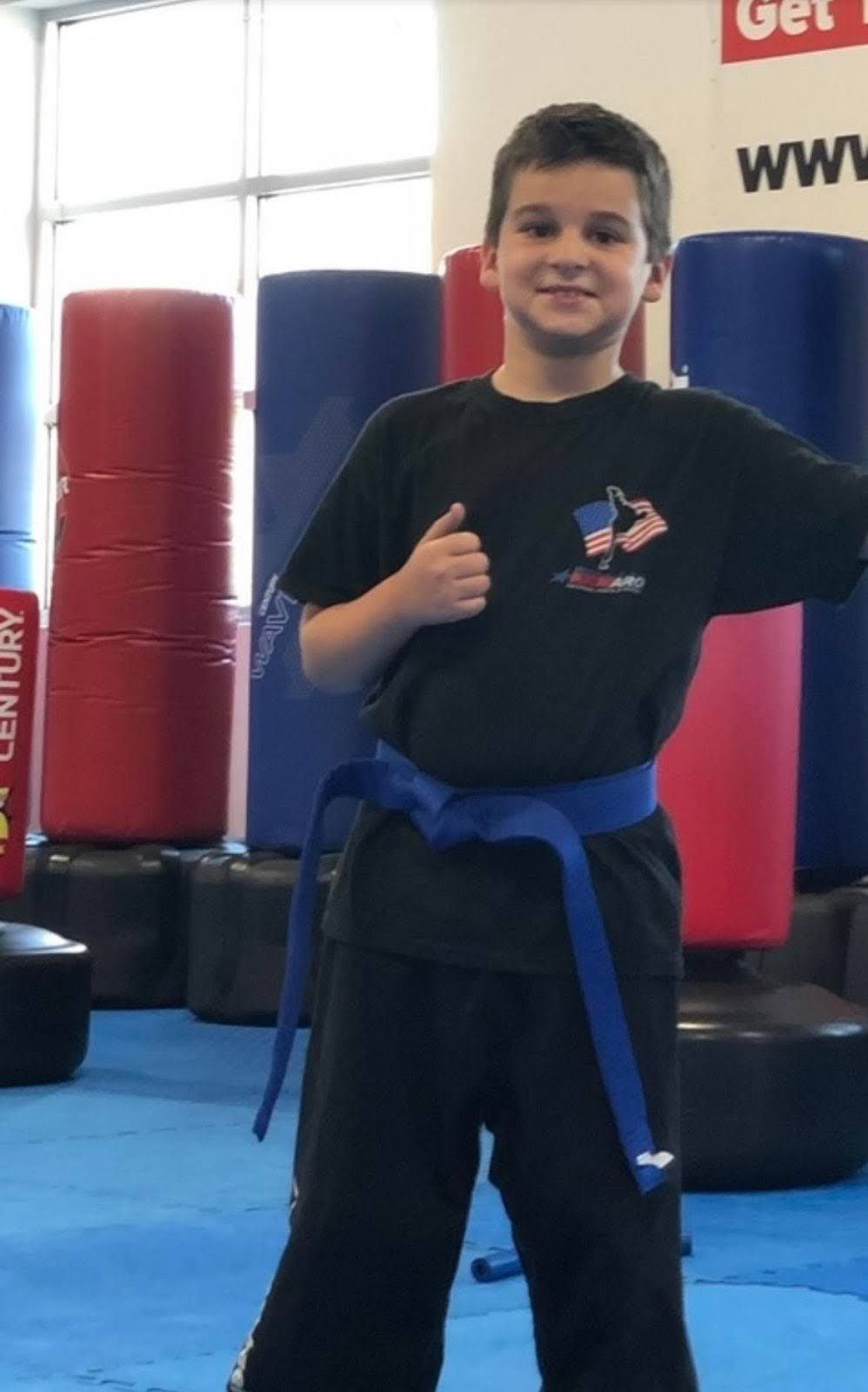 A young boy wearing a black shirt and a blue belt giving a thumbs up