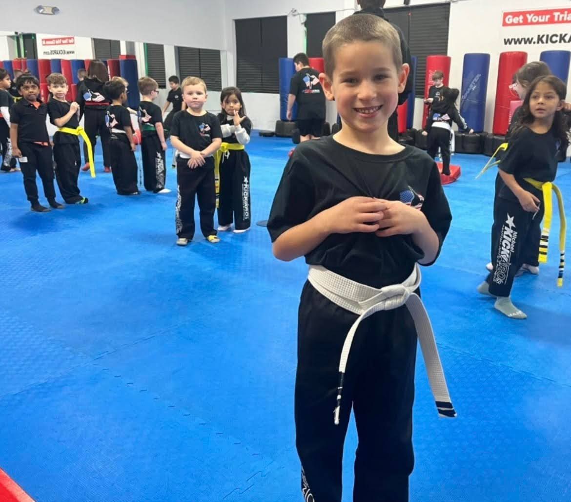 A boy with a white belt stands in front of a group of kids